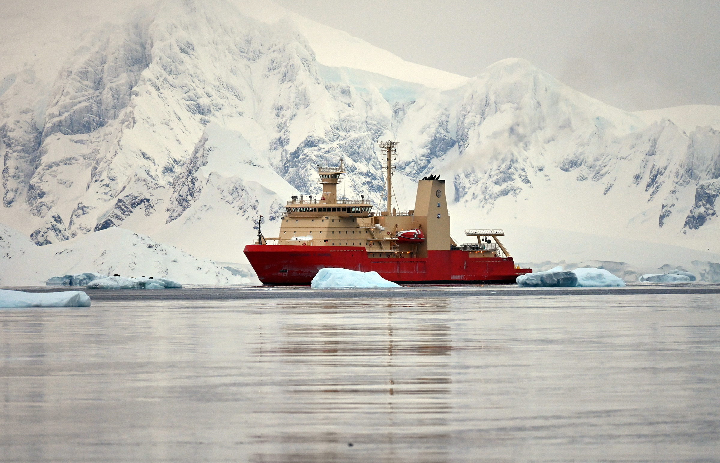 An orange and gold ship by snow-covered mountains.