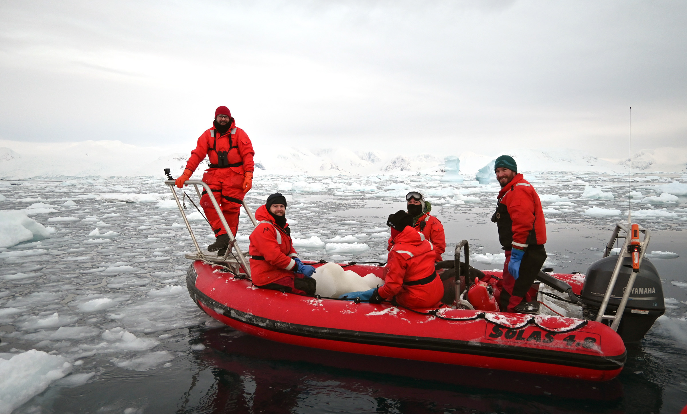 Five people in a small rubber boat in icy water.