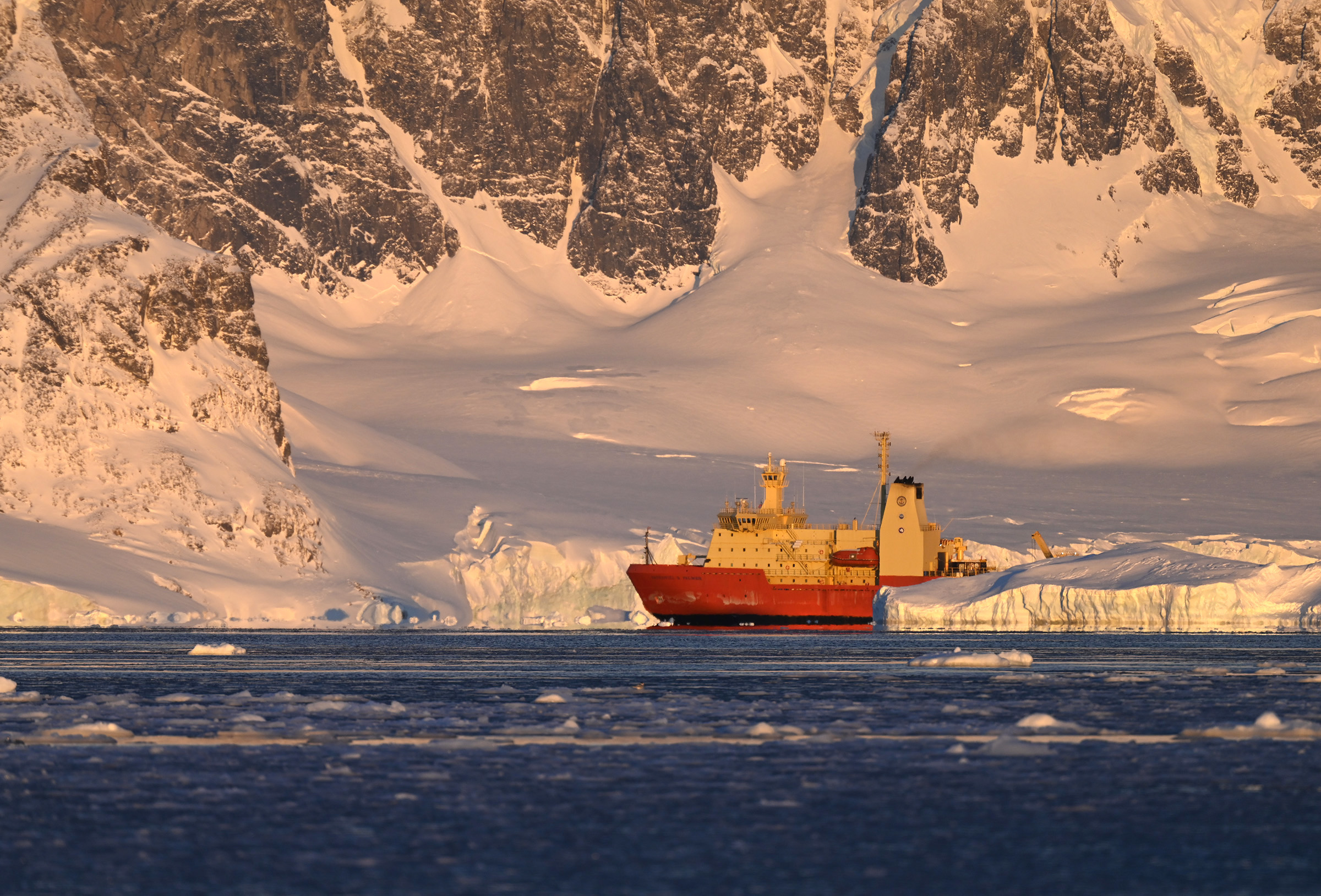 An orange and yellow ship amongst icebergs and cliffsides