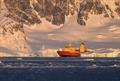An orange and yellow ship amongst icebergs and cliffsides