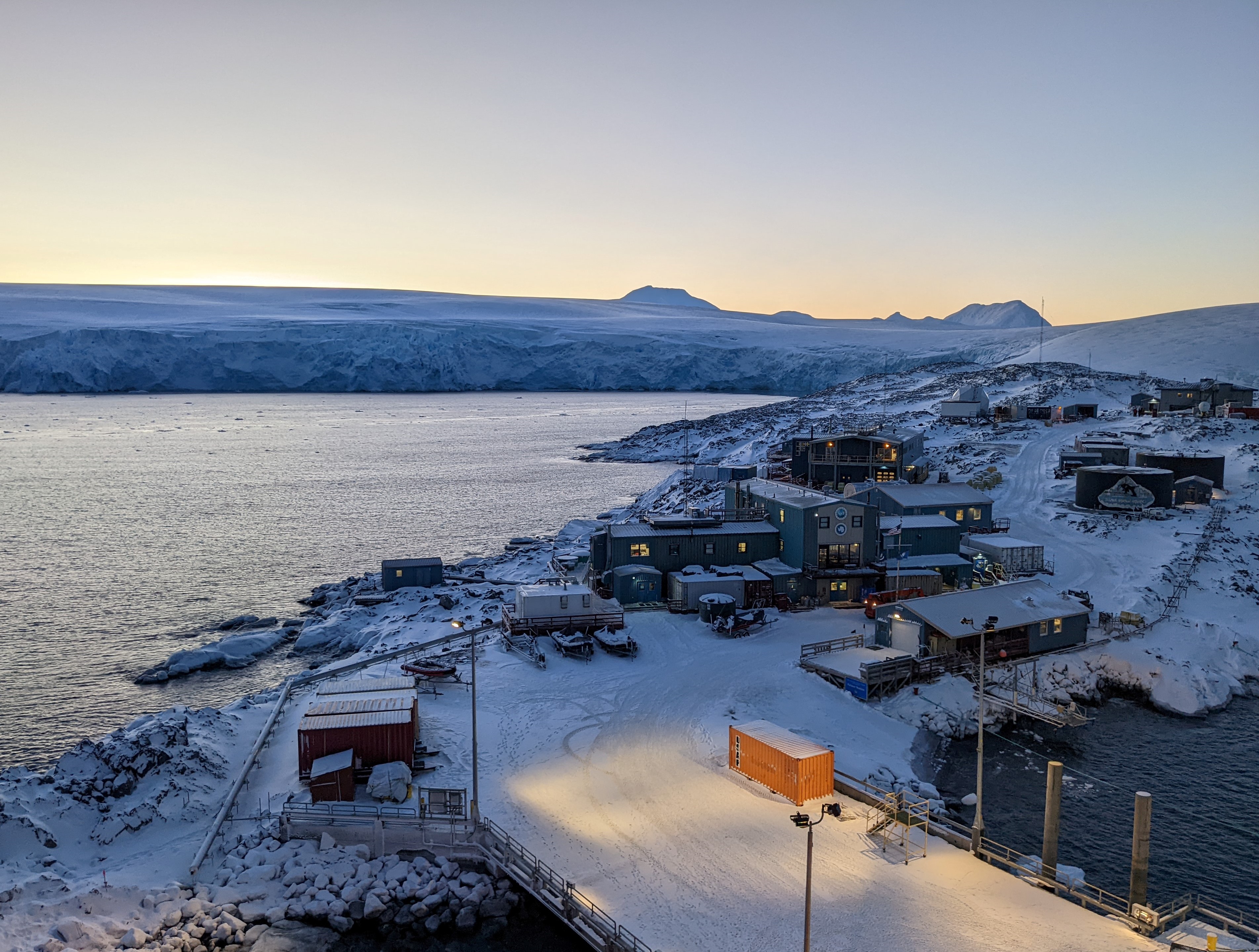 A cluster of buildings by a shoreline, with a glacier in the distance.