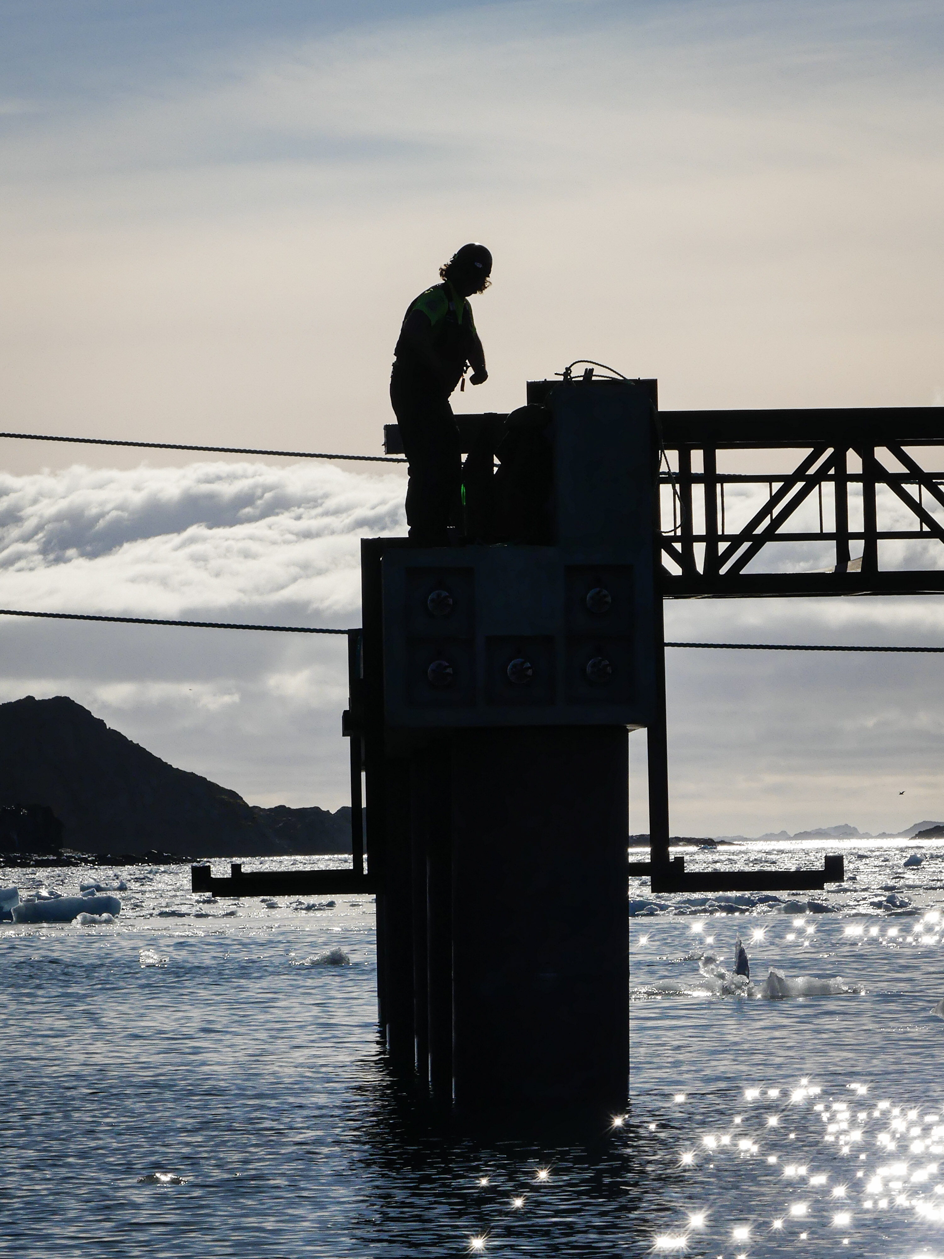 A man standing on a pier silhouetted by the setting sun. 