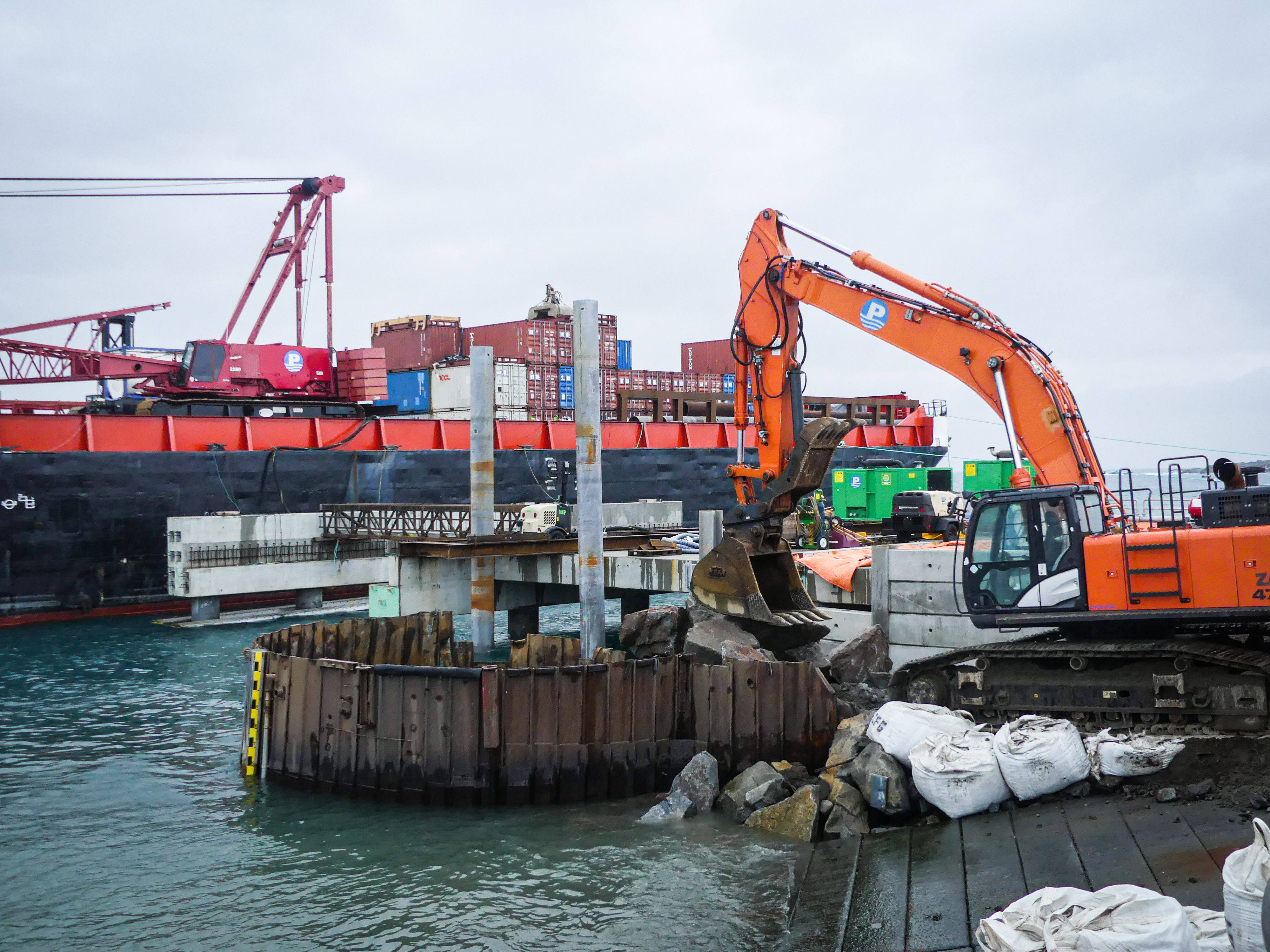 A backhoe takes apart a dirt pier and retaining wall. 