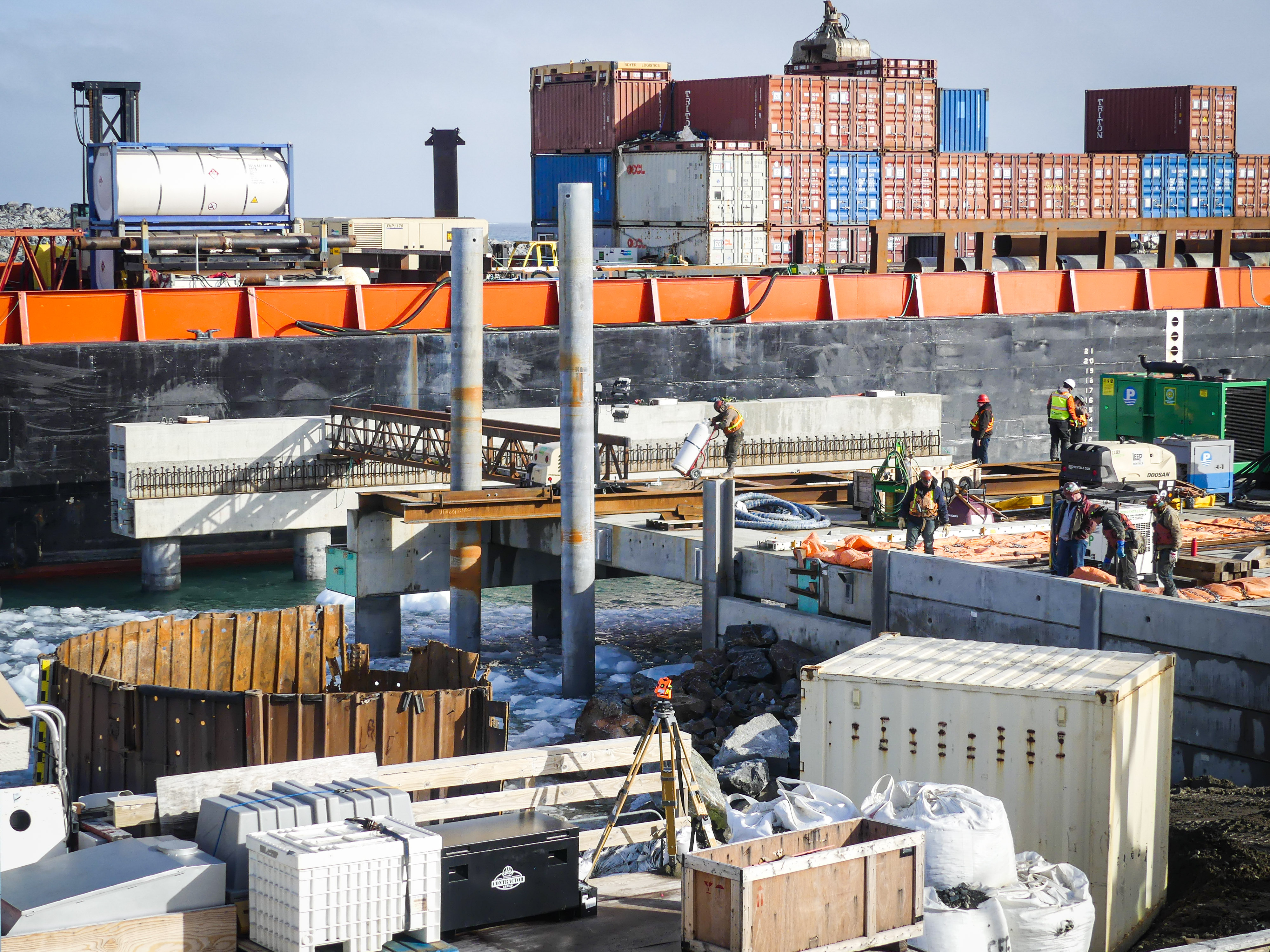 A concrete pier and steel pilings with a barge in the background. 