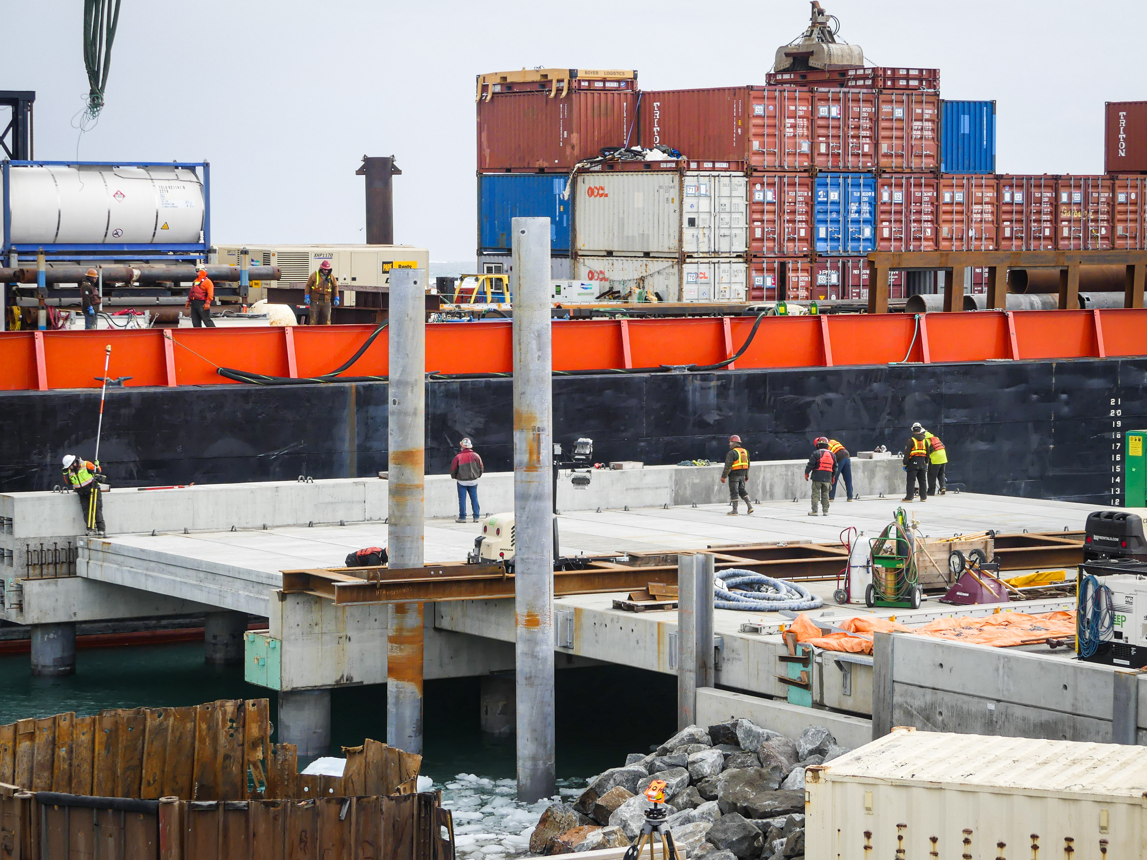 A concrete pier and steel pilings with a barge in the background. 