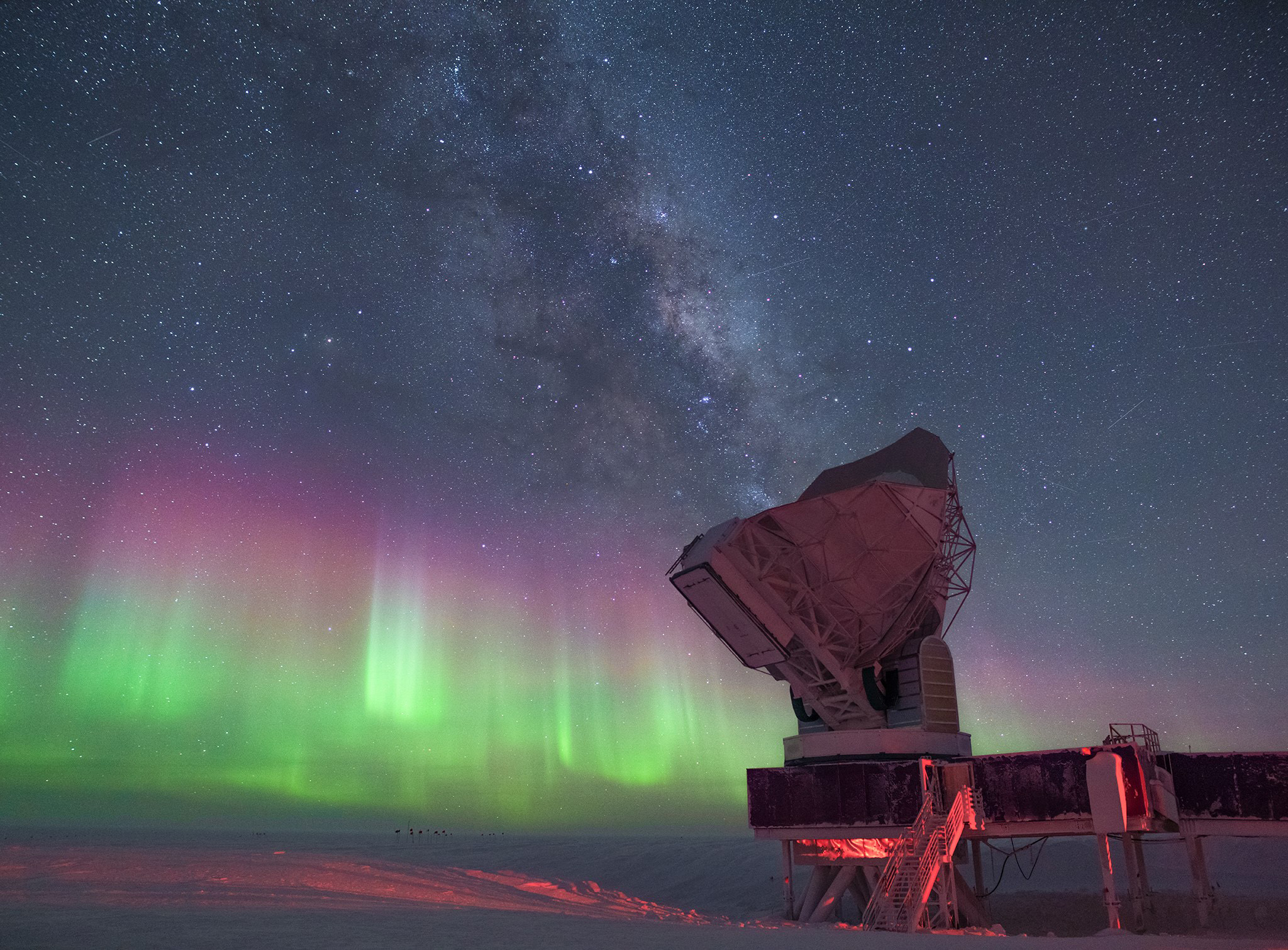 Green, pink and lavender auroras along with the Milky Way fill the sky above a large telescope.