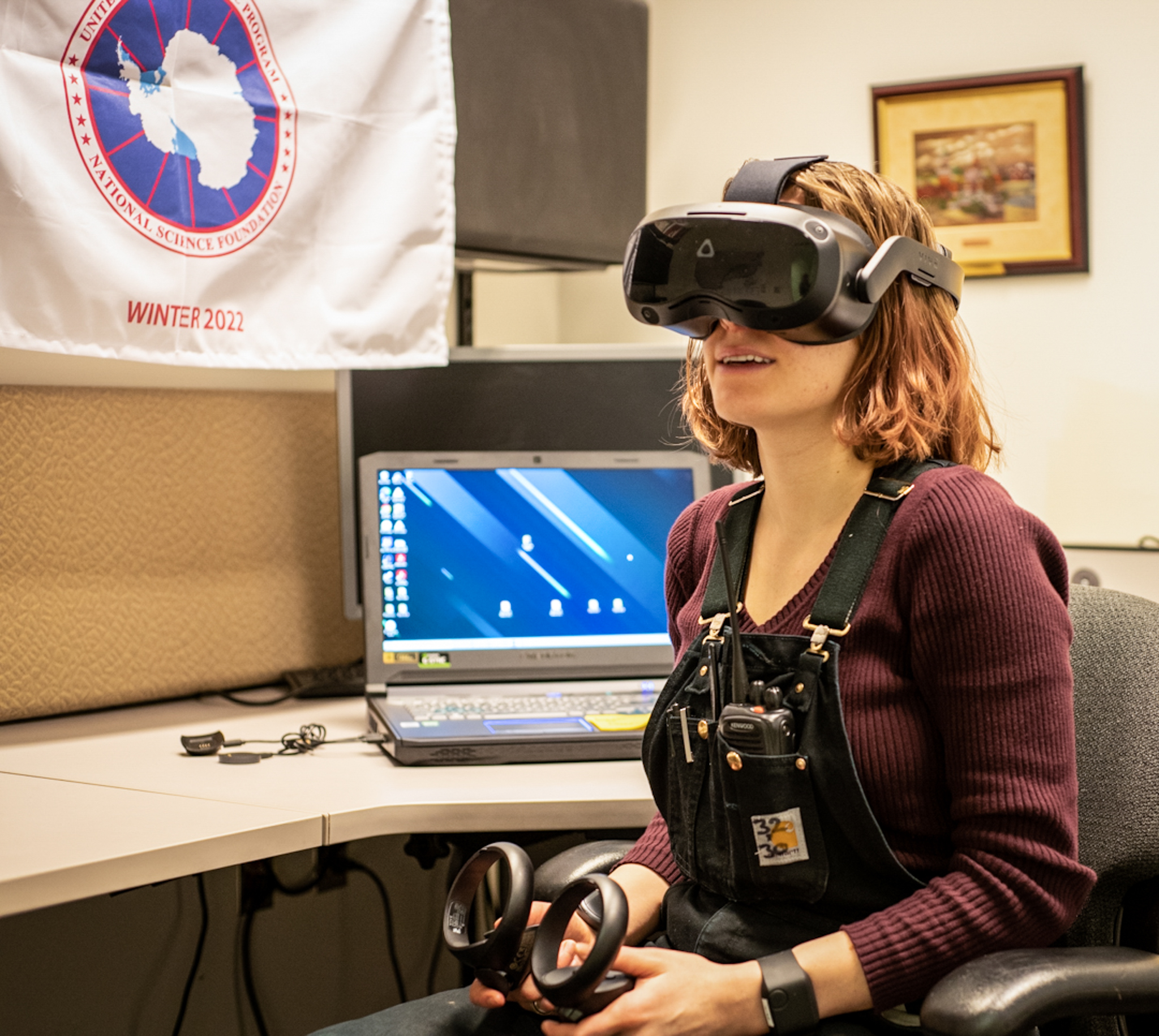 Woman with virtual reality goggles on head, sitting in front of desk and laptop