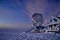 Large telescope surrounded by snow with twilight sky above