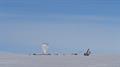 A large science balloon in the distance across snow field with crane against blue sky