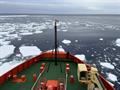 The bow of a ship in water with sea ice in front of ship.