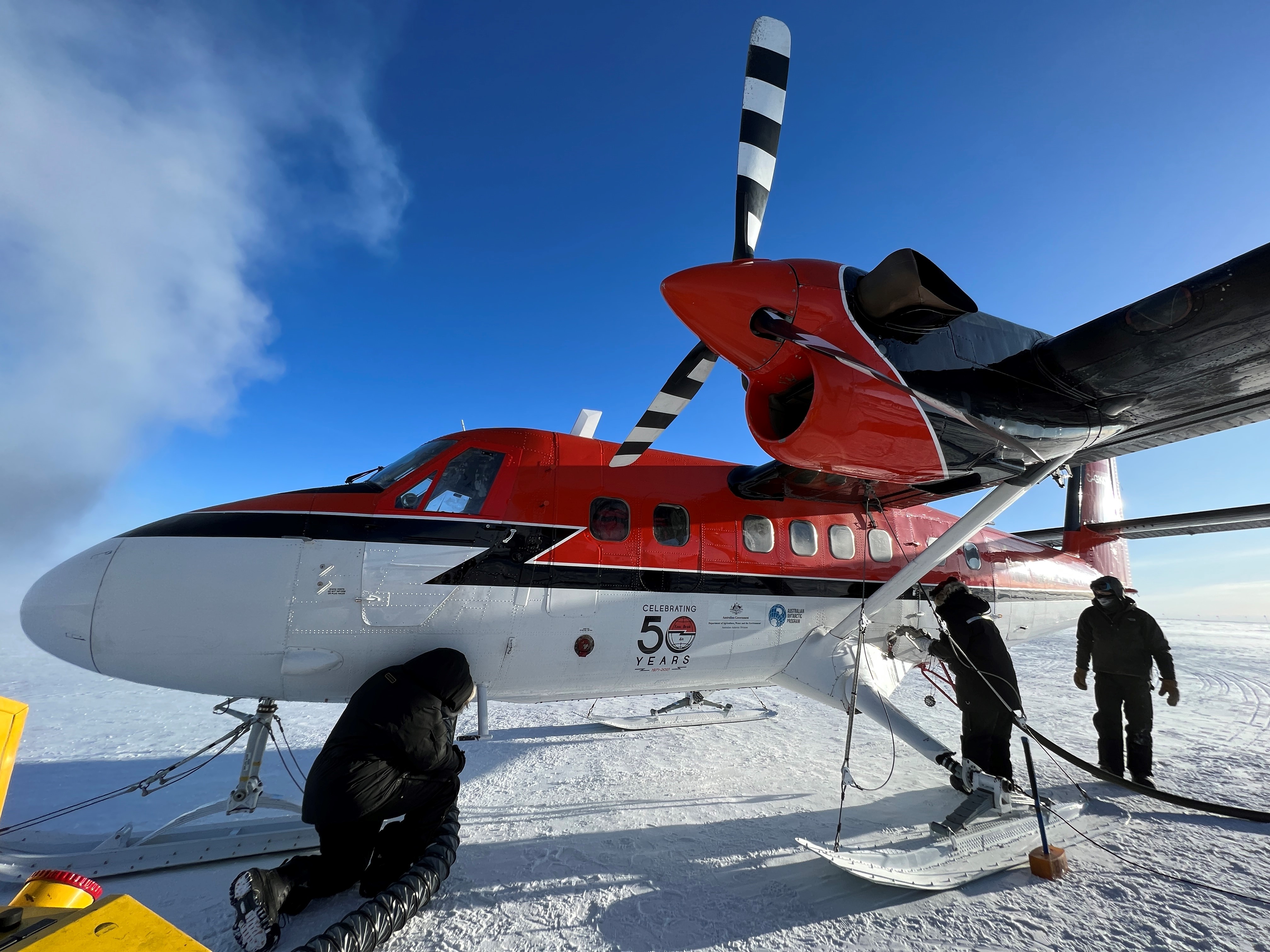 Small red and white prop plane being refueled by support staff