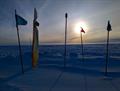 flag poles cast shadows on snowy landscape with sun low in the sky