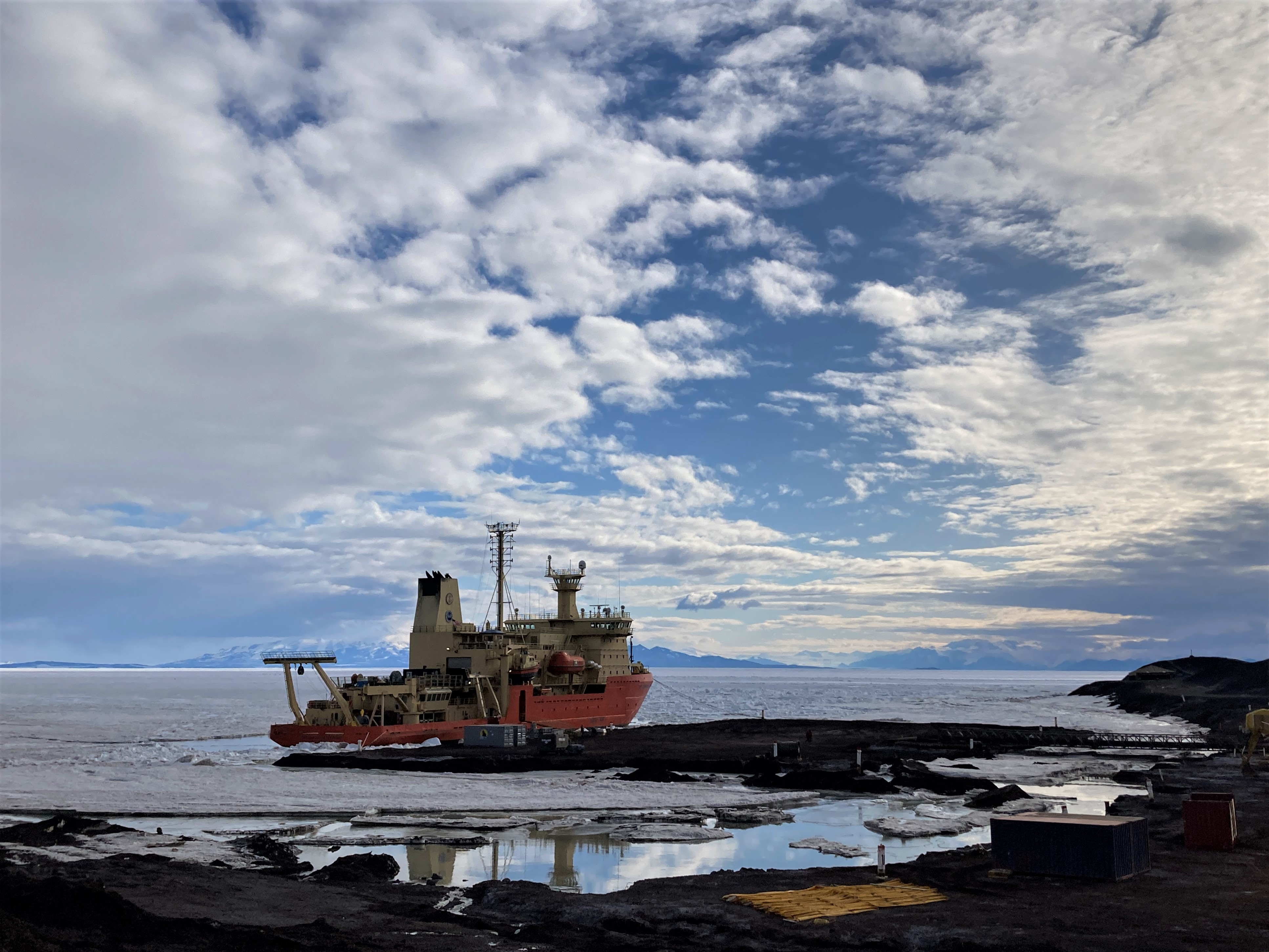 Research ship docked at pier with cloud-filled sky above.