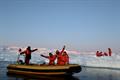A group of scientists in small boat as another group works on ice floe in background.