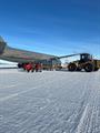 Workers load large cargo plane on snow runway with large tractor in foreground