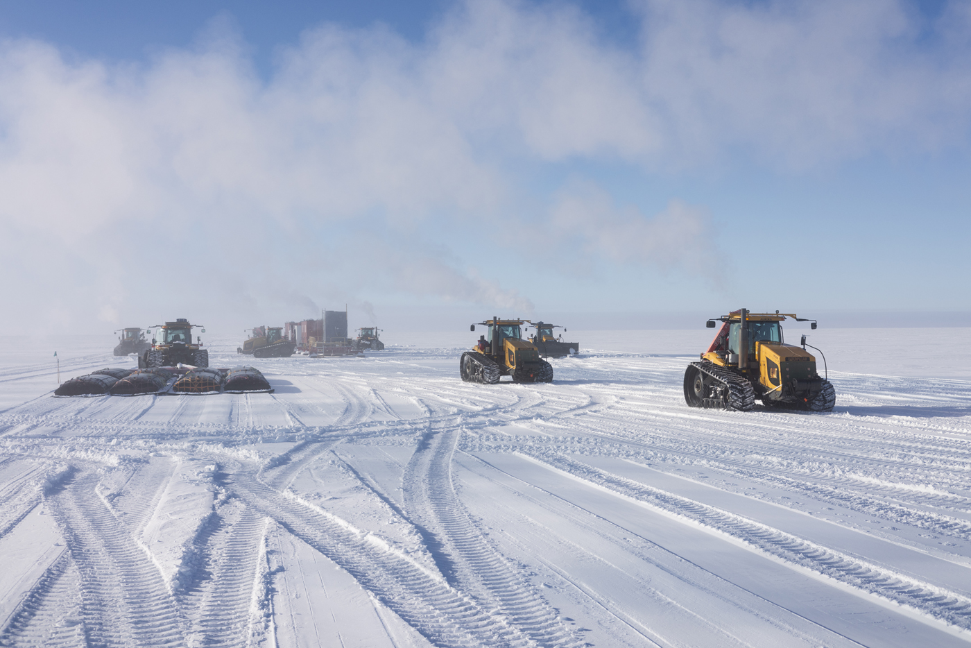 Tractors spread across a snowy landscape with mist hanging above in front of blue sky.