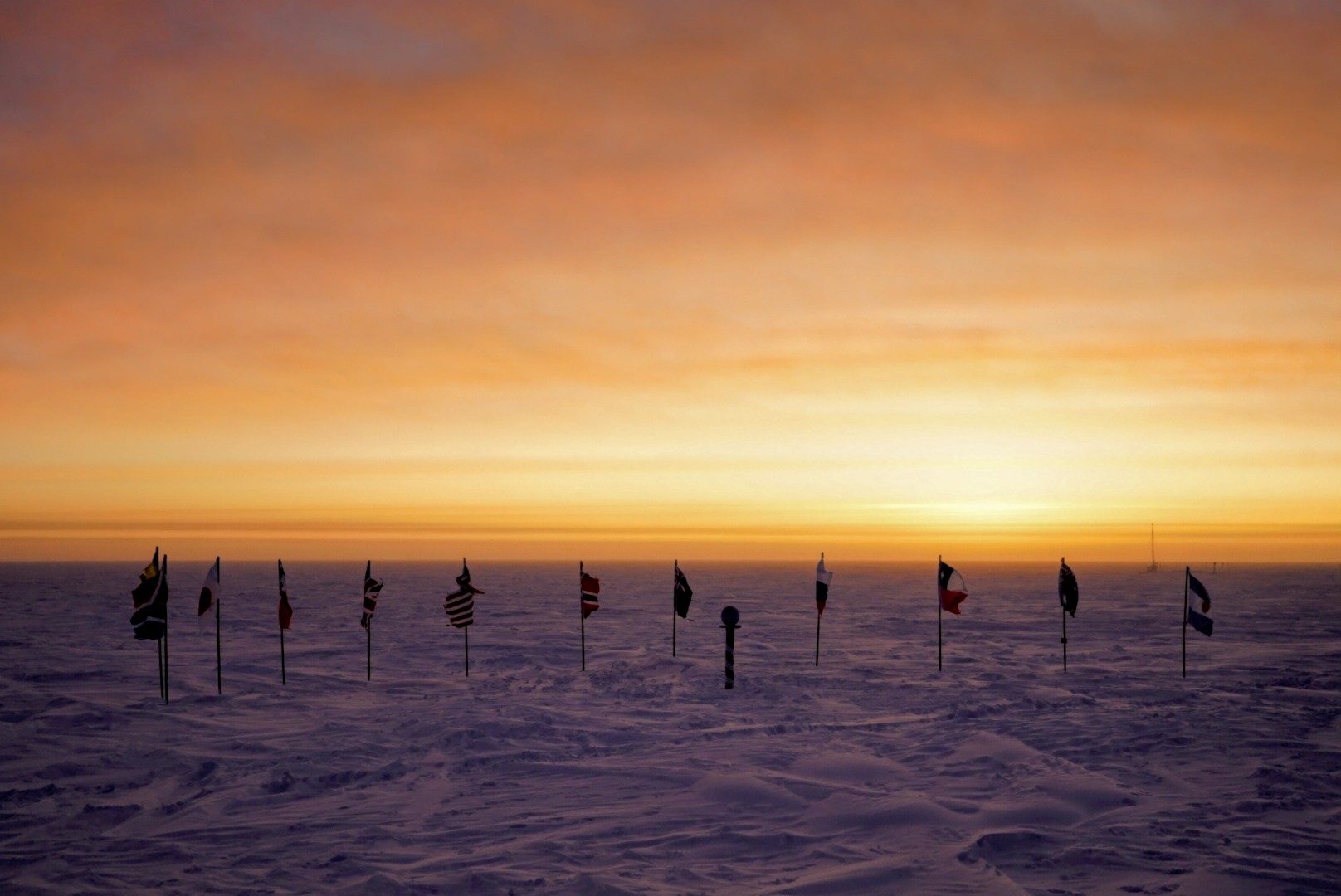 A row of flags planted in snow silhouetted against an orange sky. 