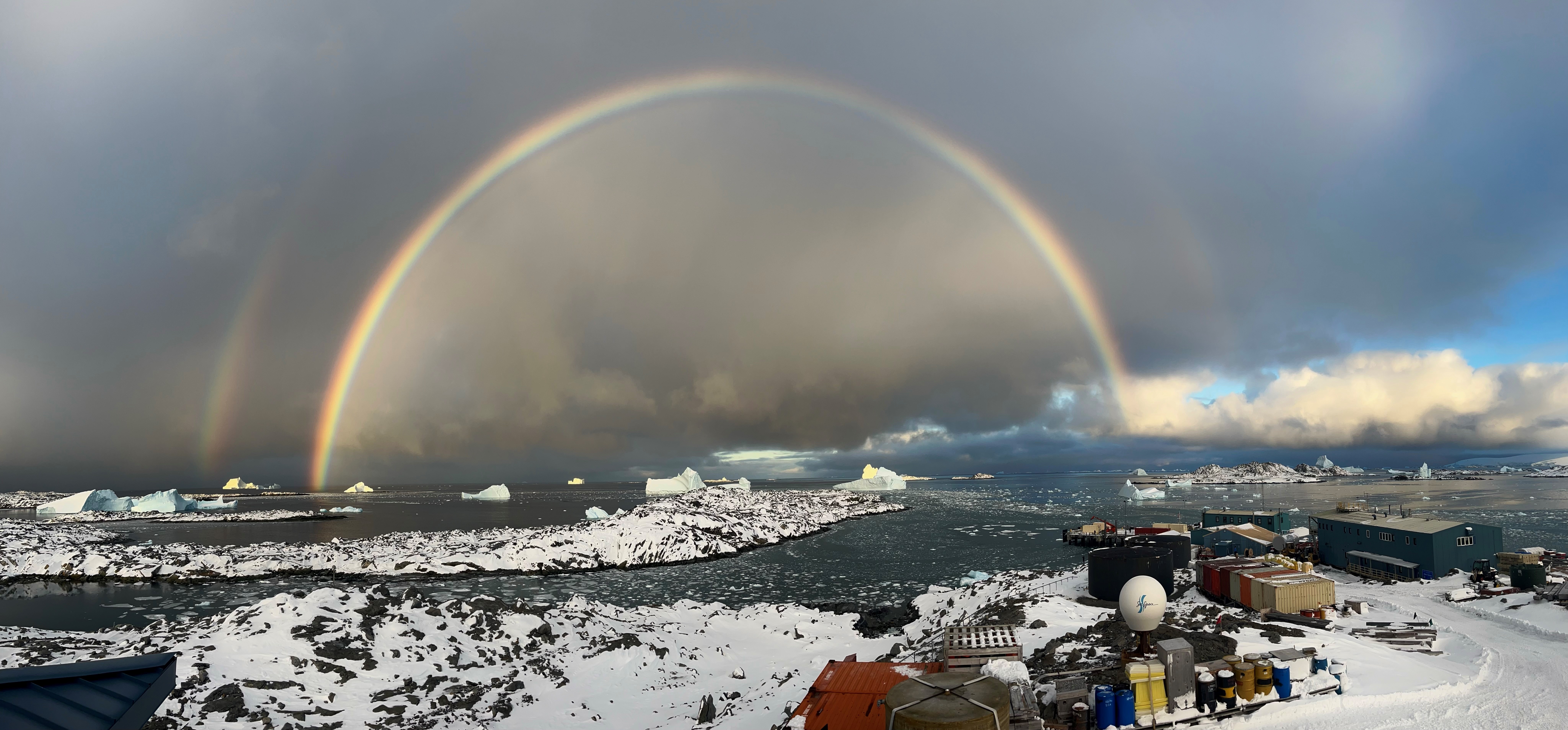 A rainbow arcs across dark clouds over a snowy landscape.