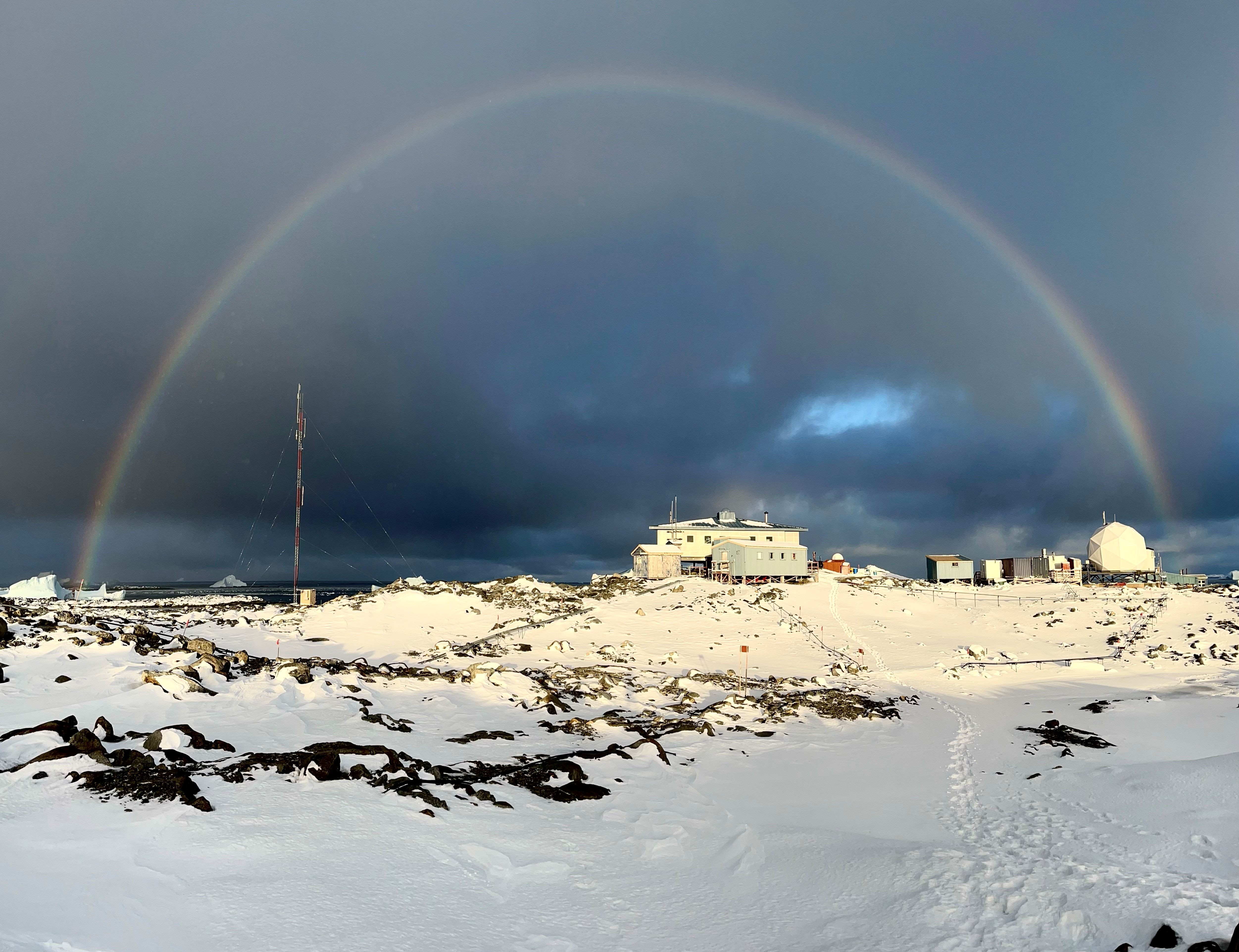 A rainbow arcs across dark clouds over a snowy landscape.