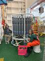 Two women work on ocean monitoring equipment on the deck of a ship