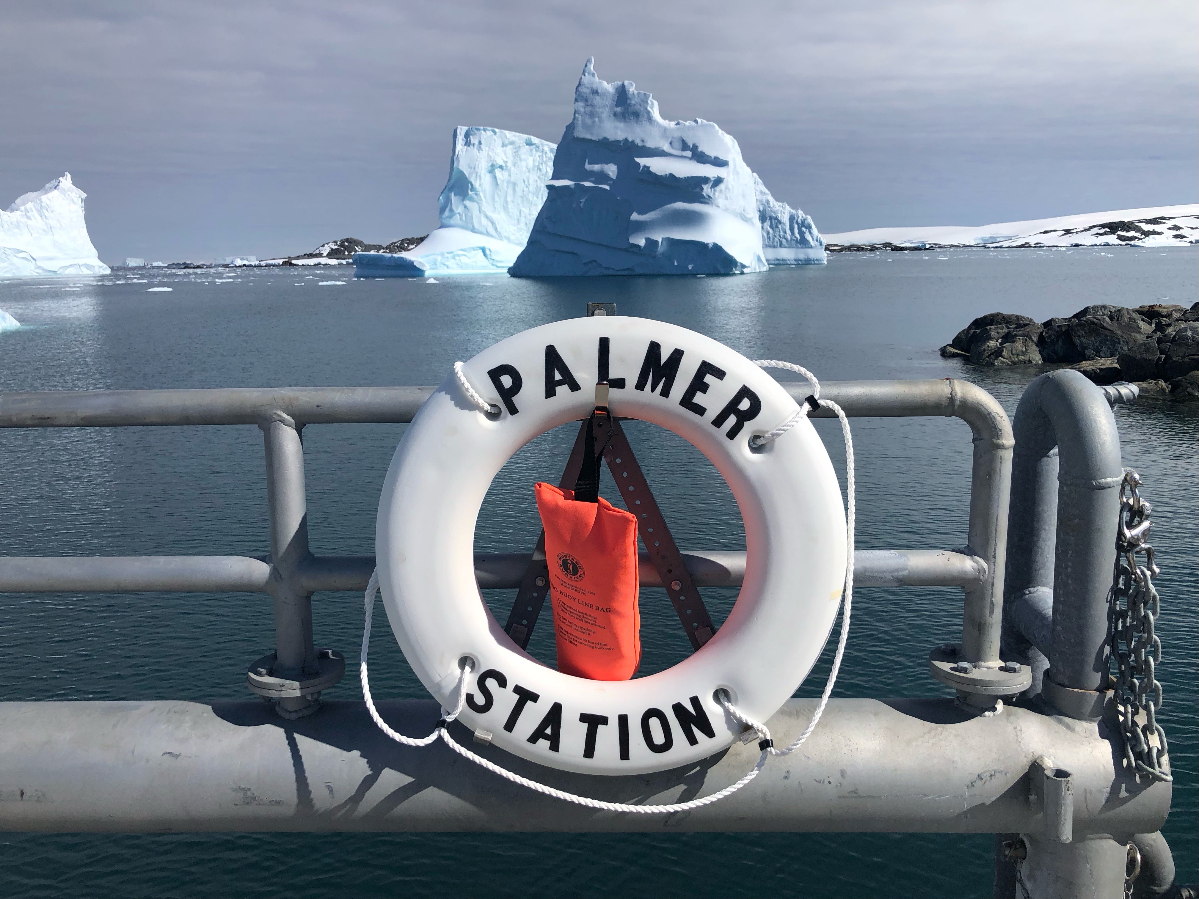 A life preserver attached to railing with water and iceberg in background.