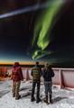 People on the deck of a ship observing auroras in the night sky.