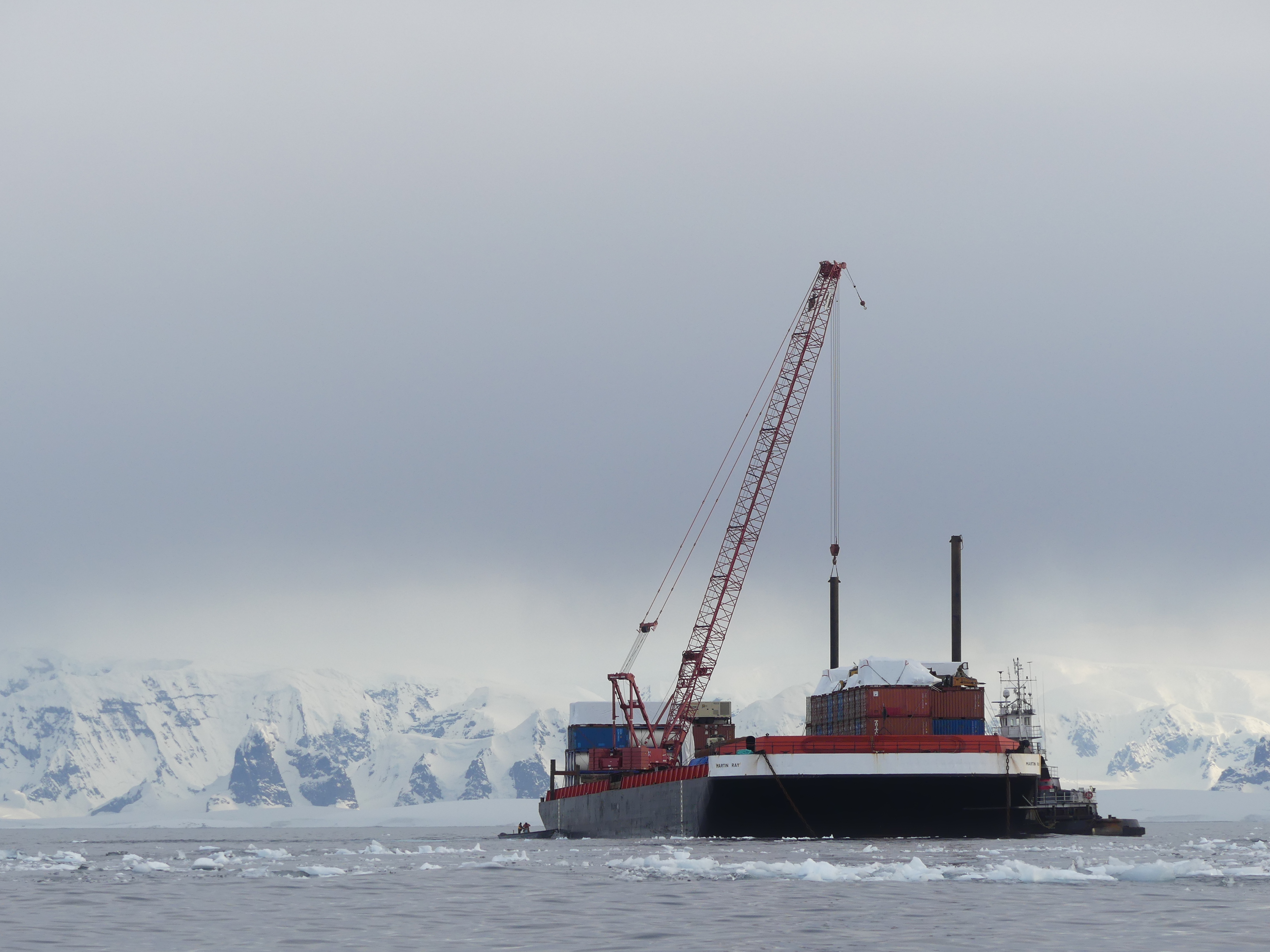 A barge and a tugboat in the ocean with mountains in the background. 