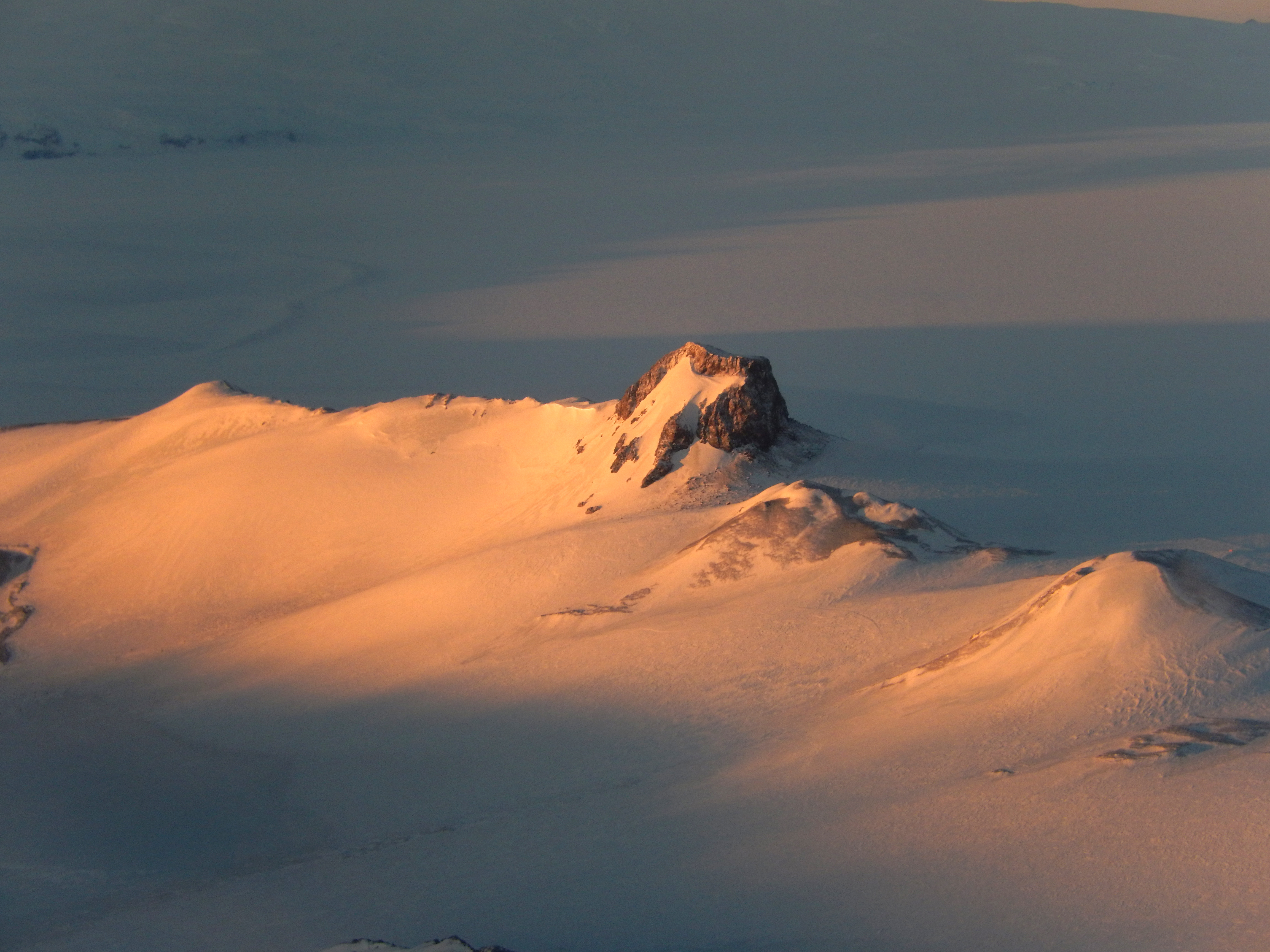 A view of a rocky outcropping in a snowy landscape at sunset.