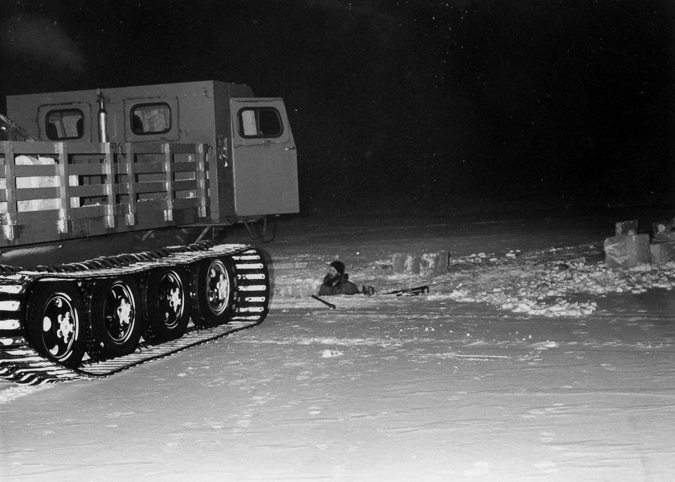 A person digging snow and ice near a tracked vehicle.