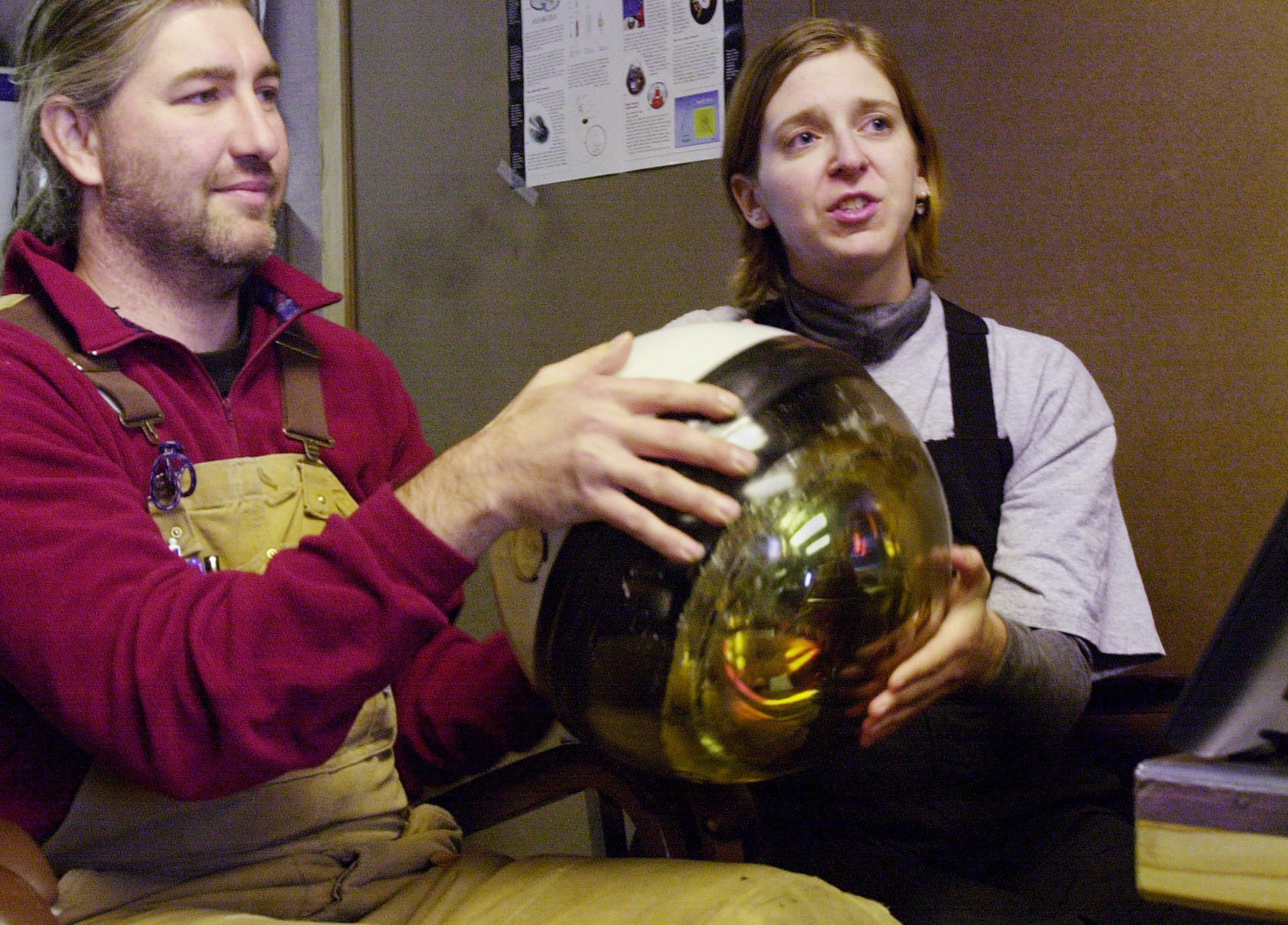 A man and woman seated, holding up a sphere while describing it.