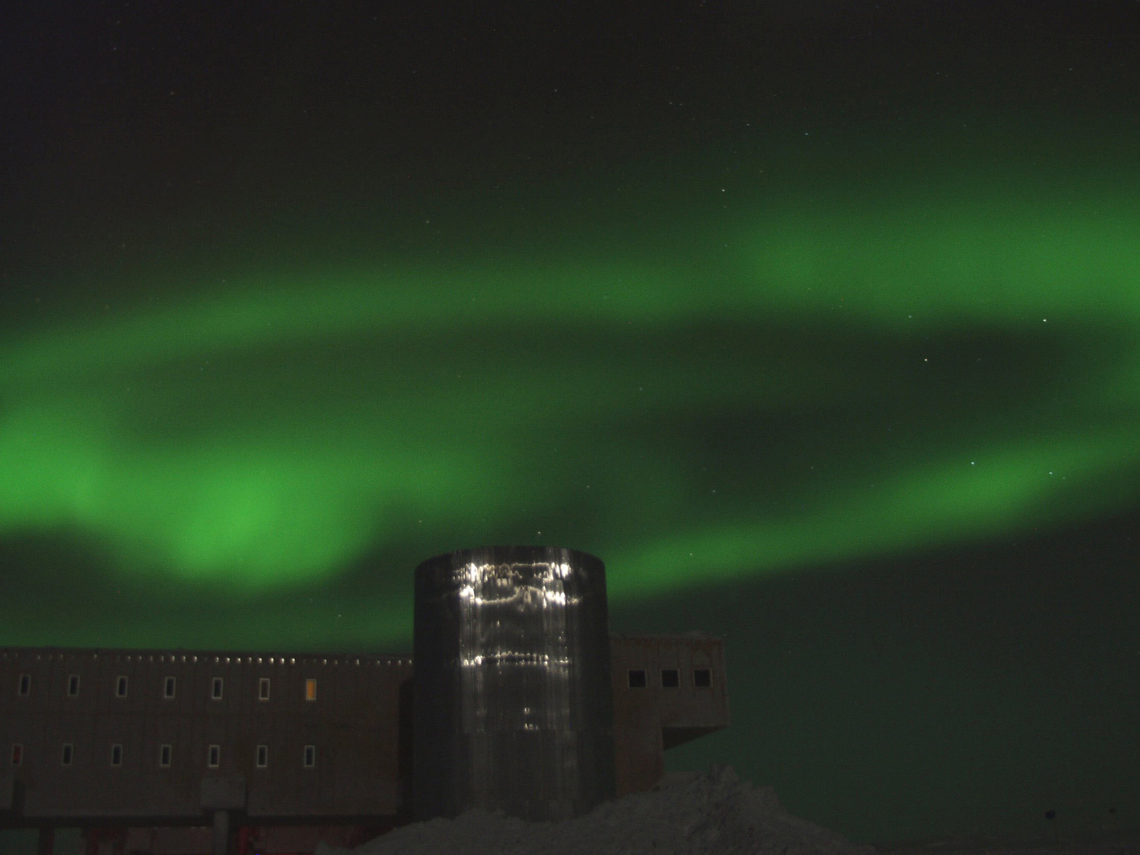 Green lights in night sky above a building at the South Pole.