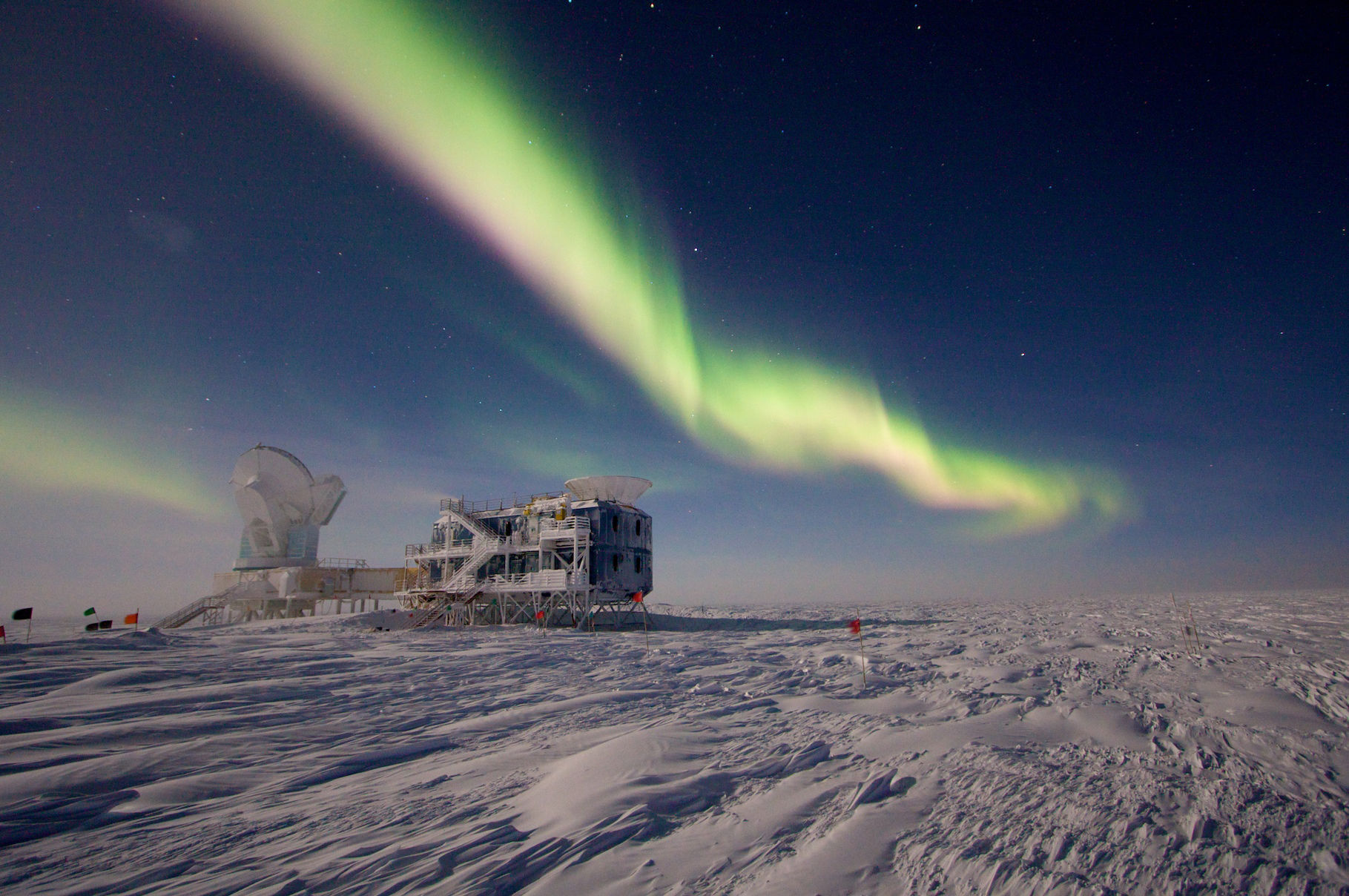 Auroras in the night sky over a science building and telescope at the U.S. research station at the geographic South Pole.