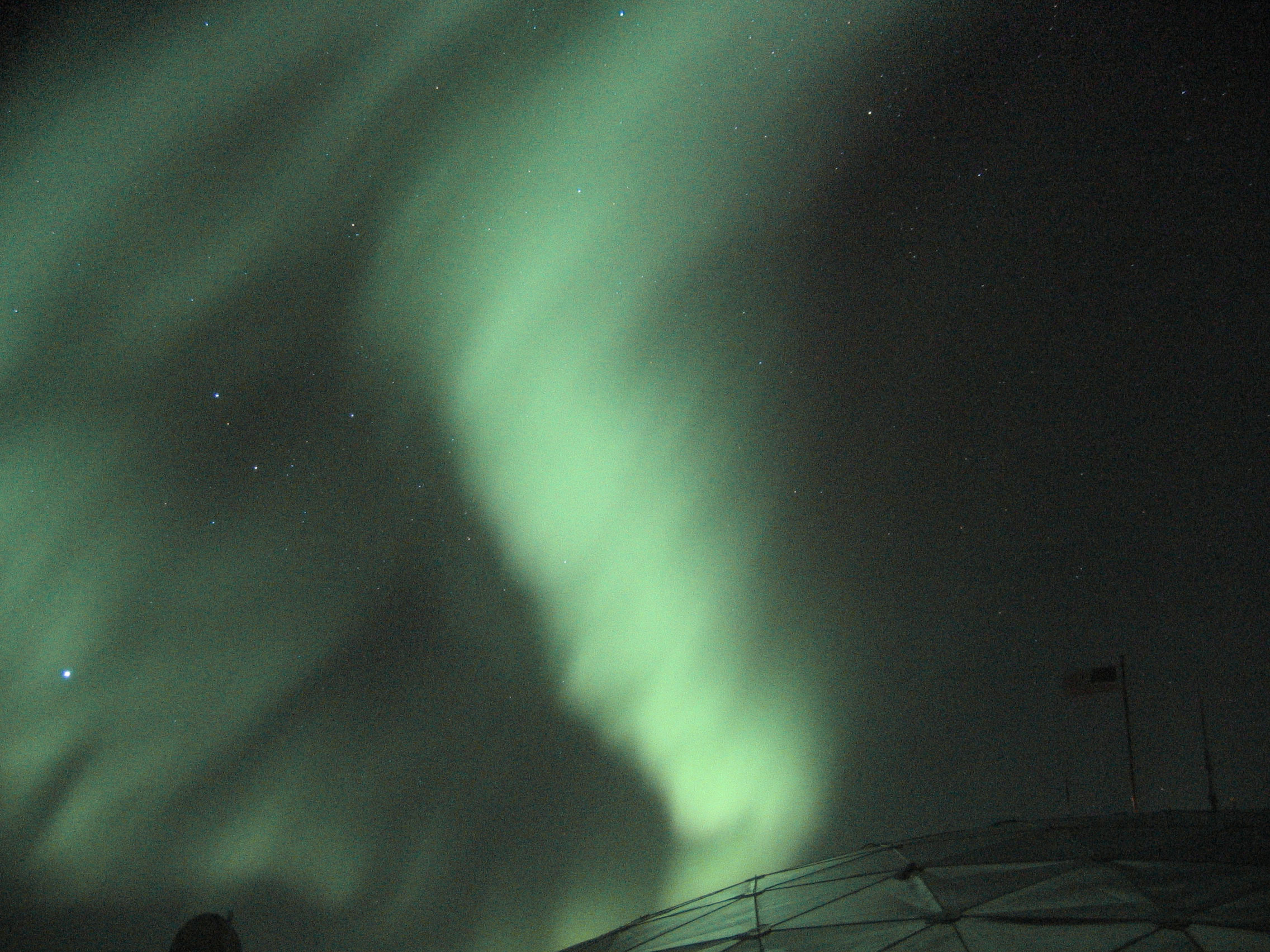 An aurora appears above a dome-shaped building at the South Pole.