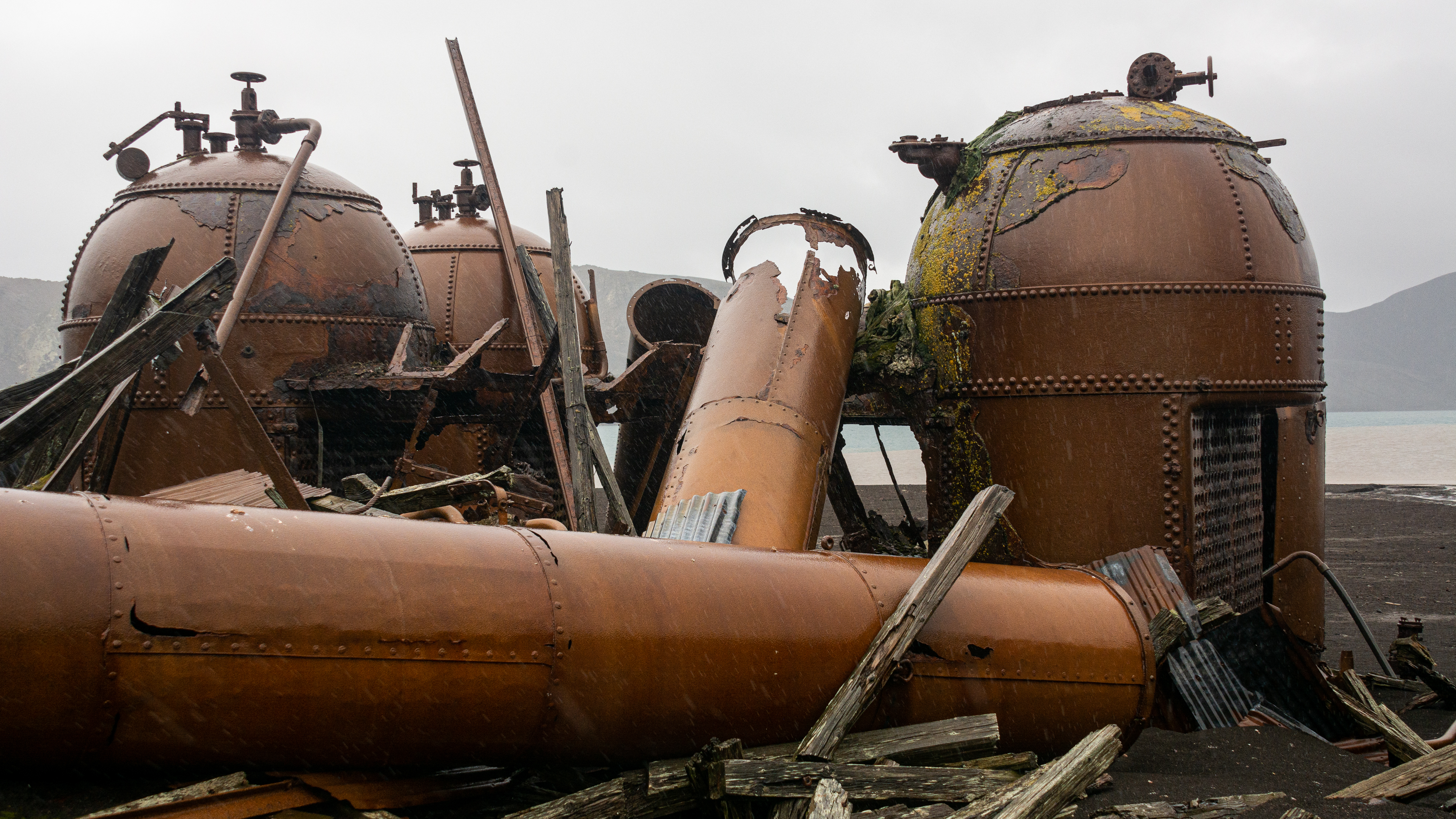 A cluster of rusting structures and pipes in the rain. 