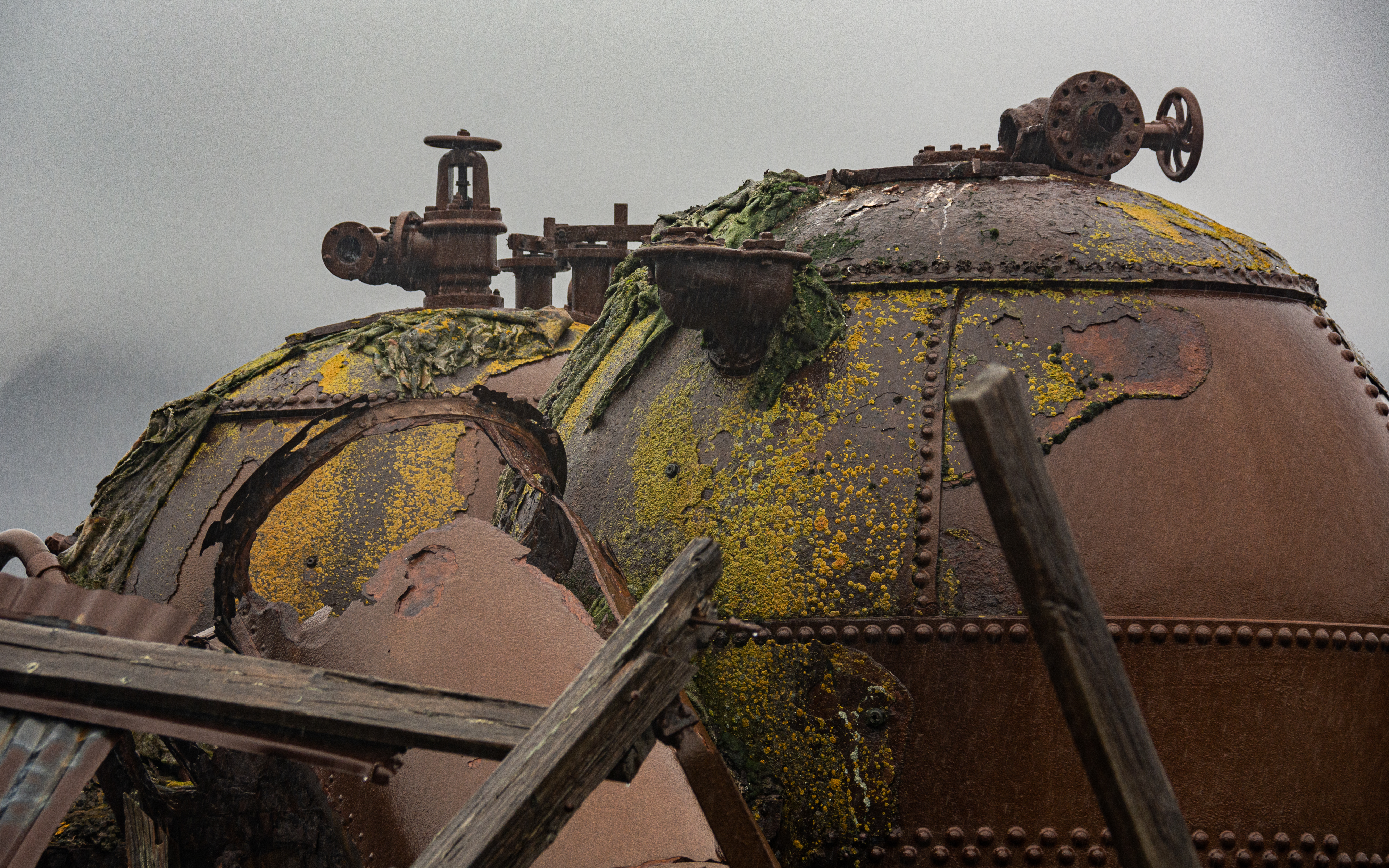 A cluster of rusting structures and pipes in the rain. 