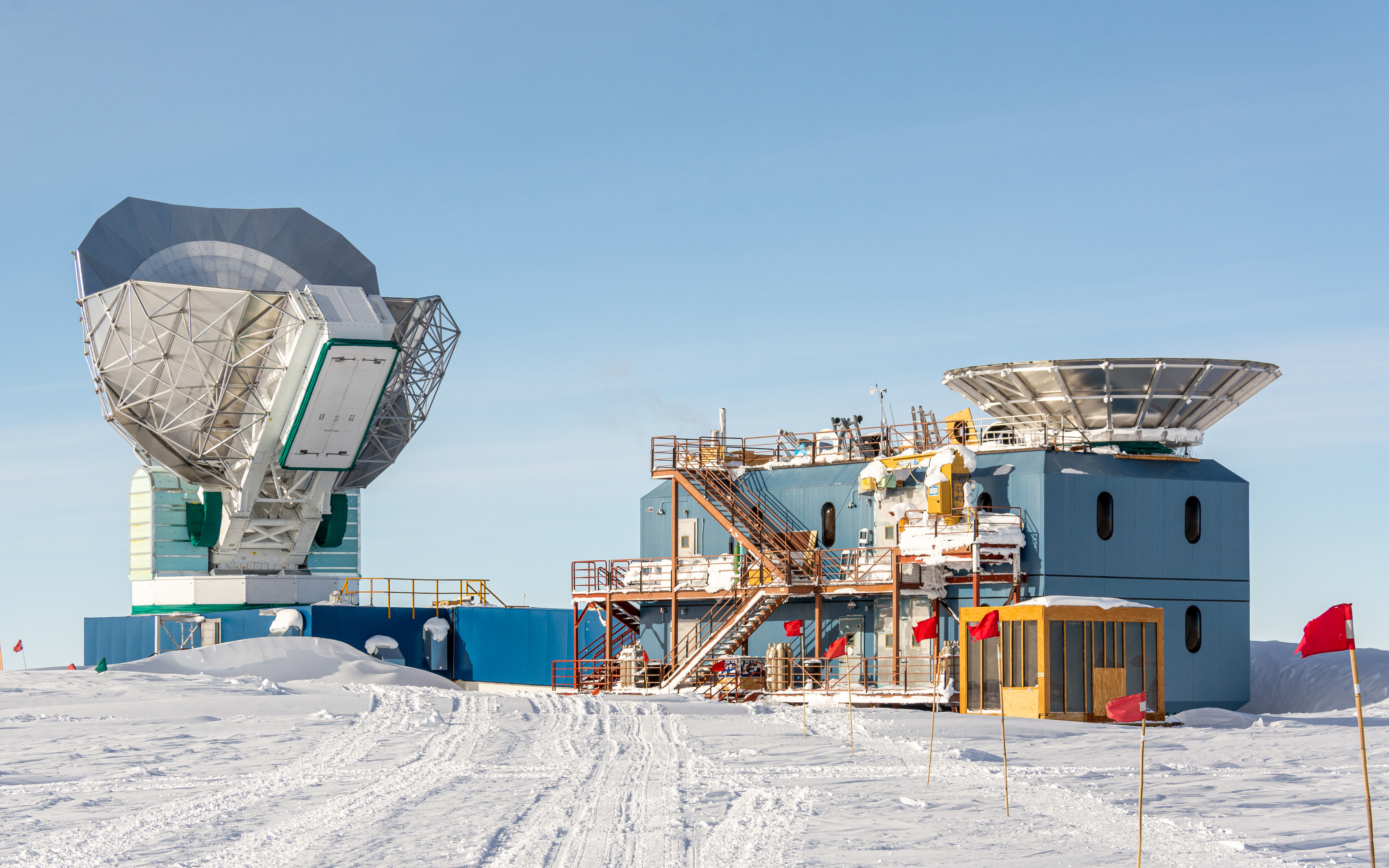 A radio telescope atop a building in a snowy landscape.