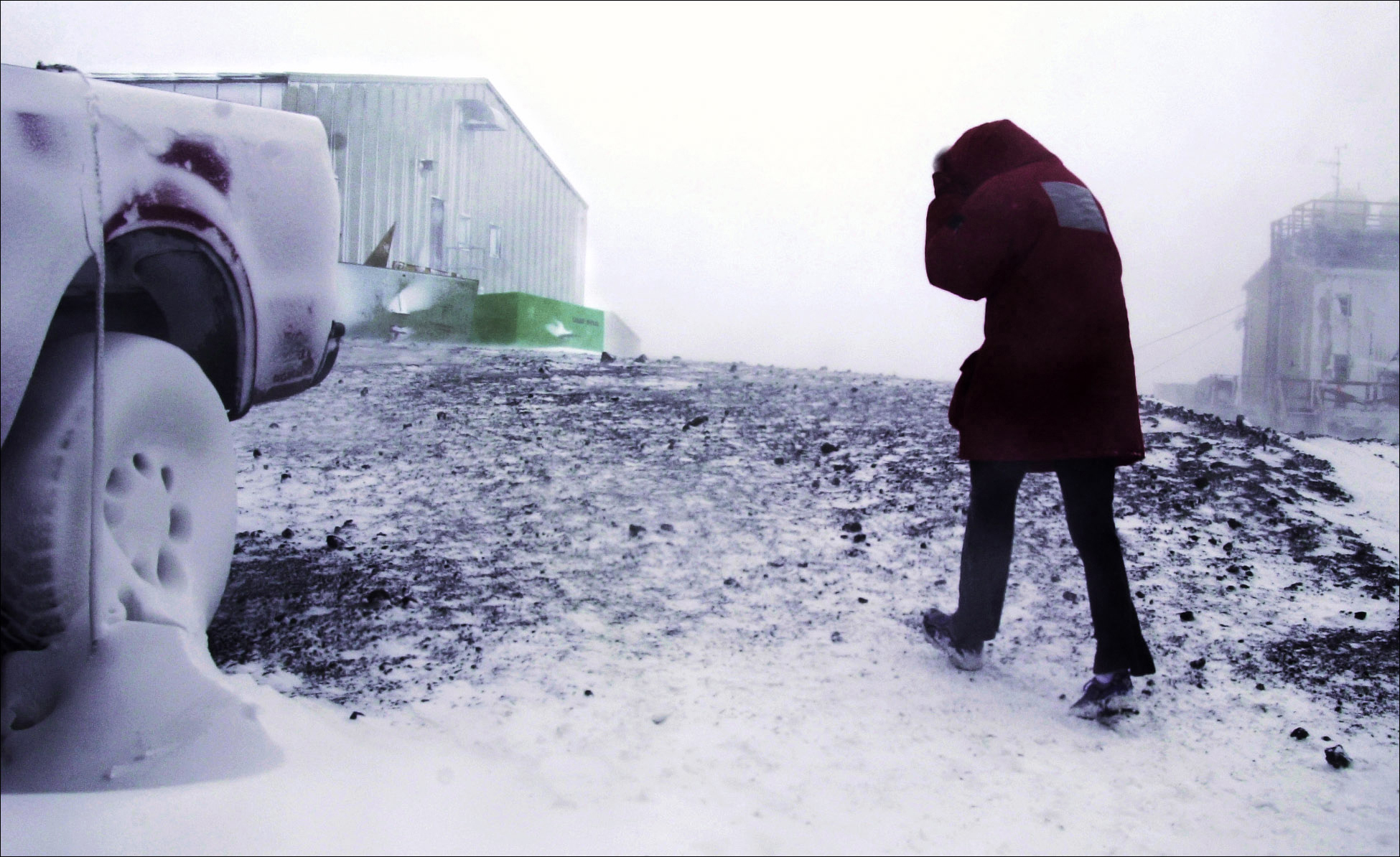 A man in a parka cowers in the wind.