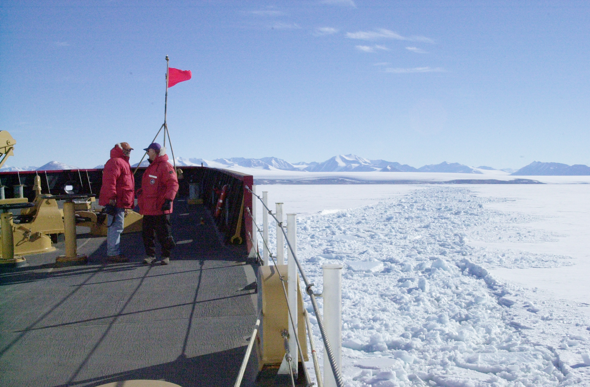 Two people stand on the bow of a ship in ice.