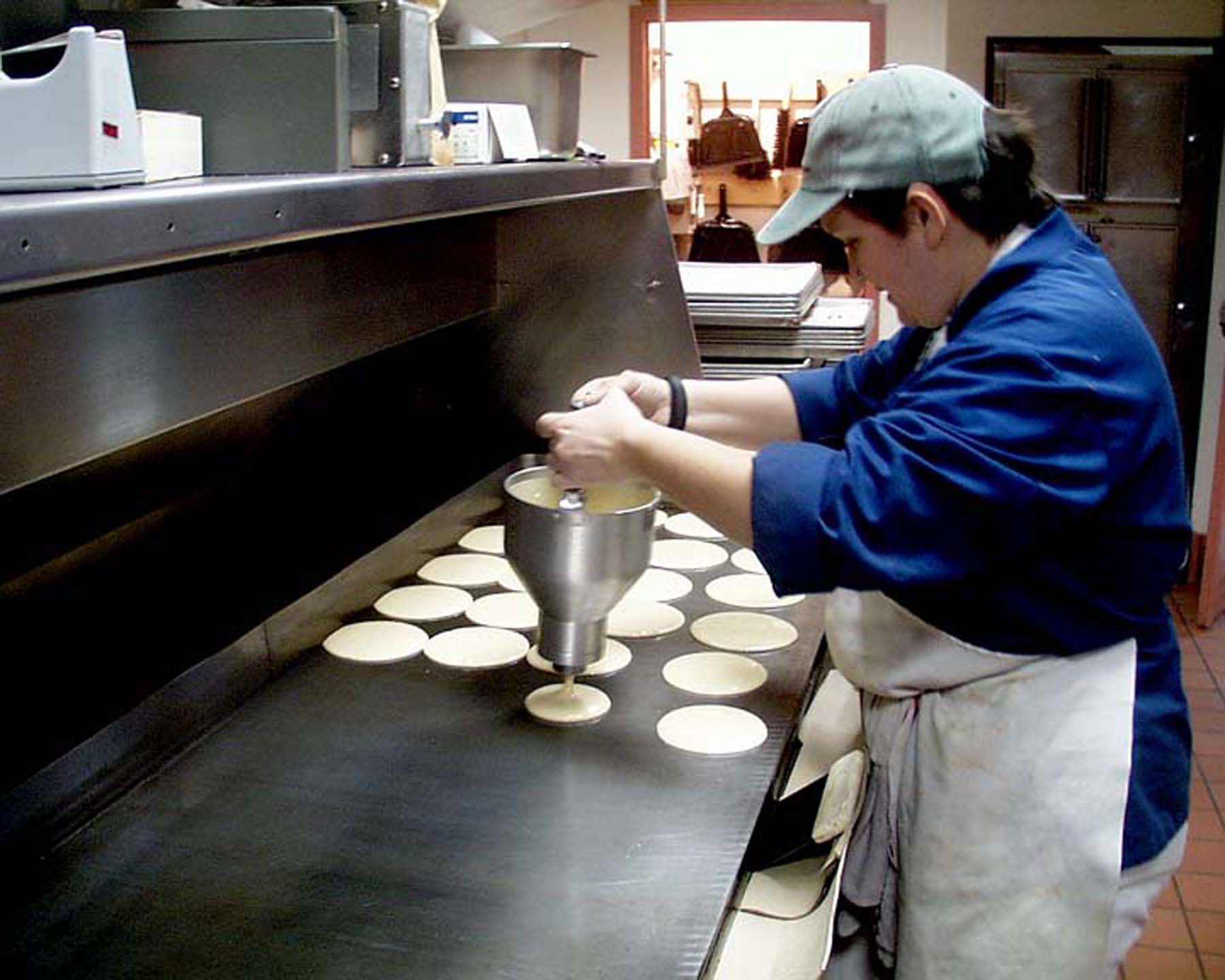 A person pours pancake batter onto an enormous griddle.