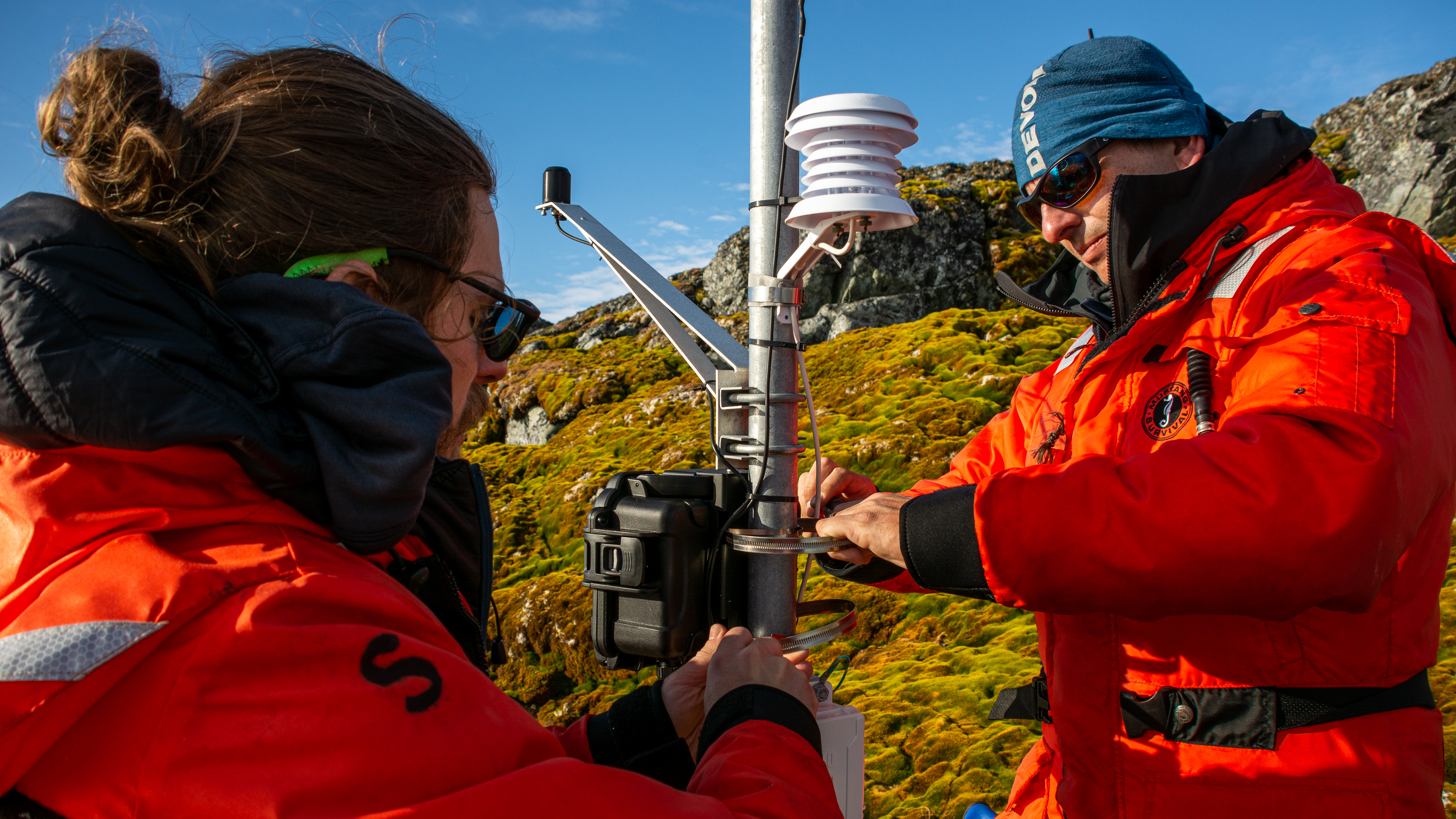 Two people install equipment onto a pole.