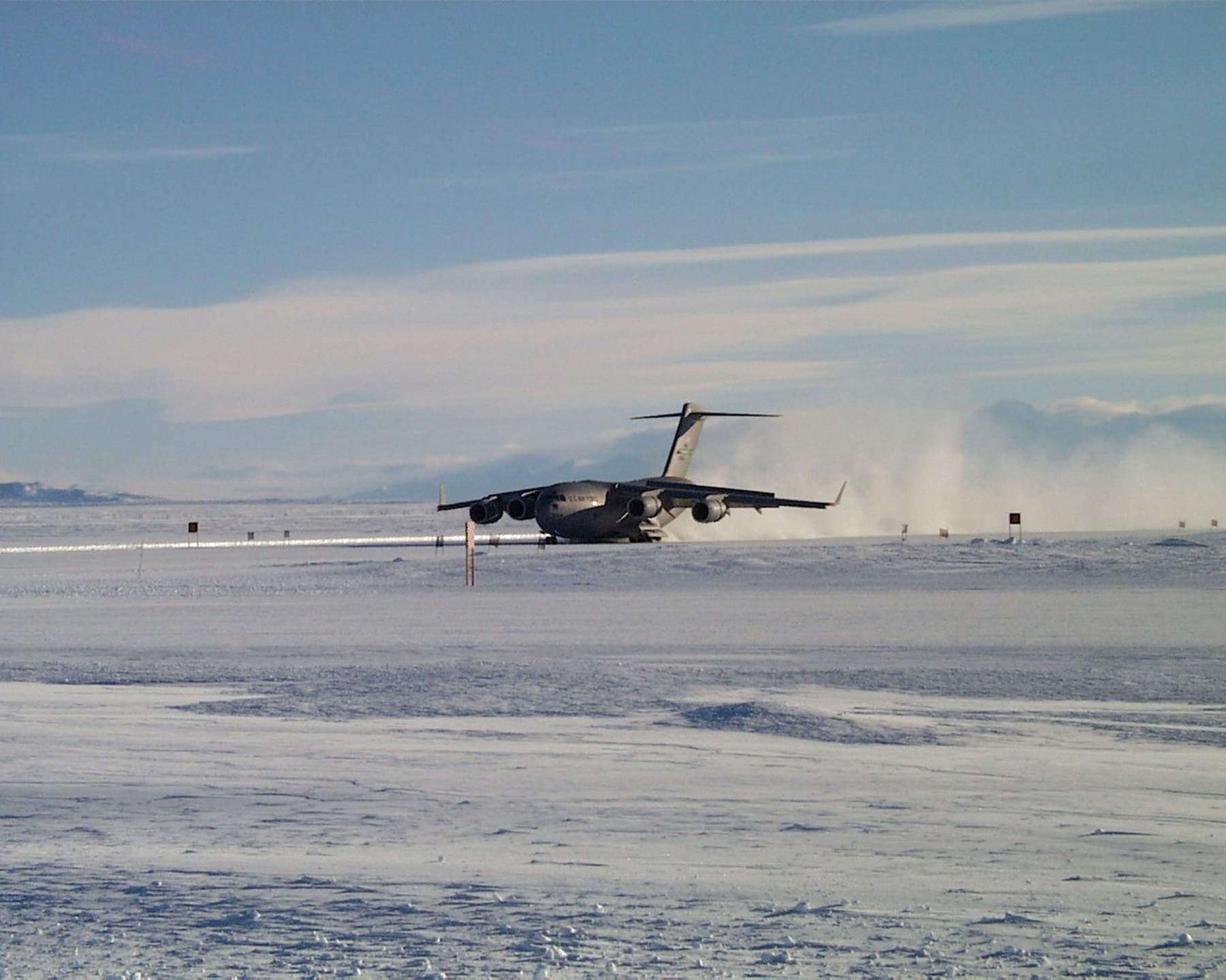 A large military jet lands on an ice runway.