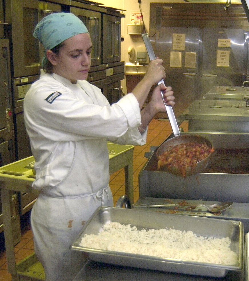 Woman pours food over into pan of rice.