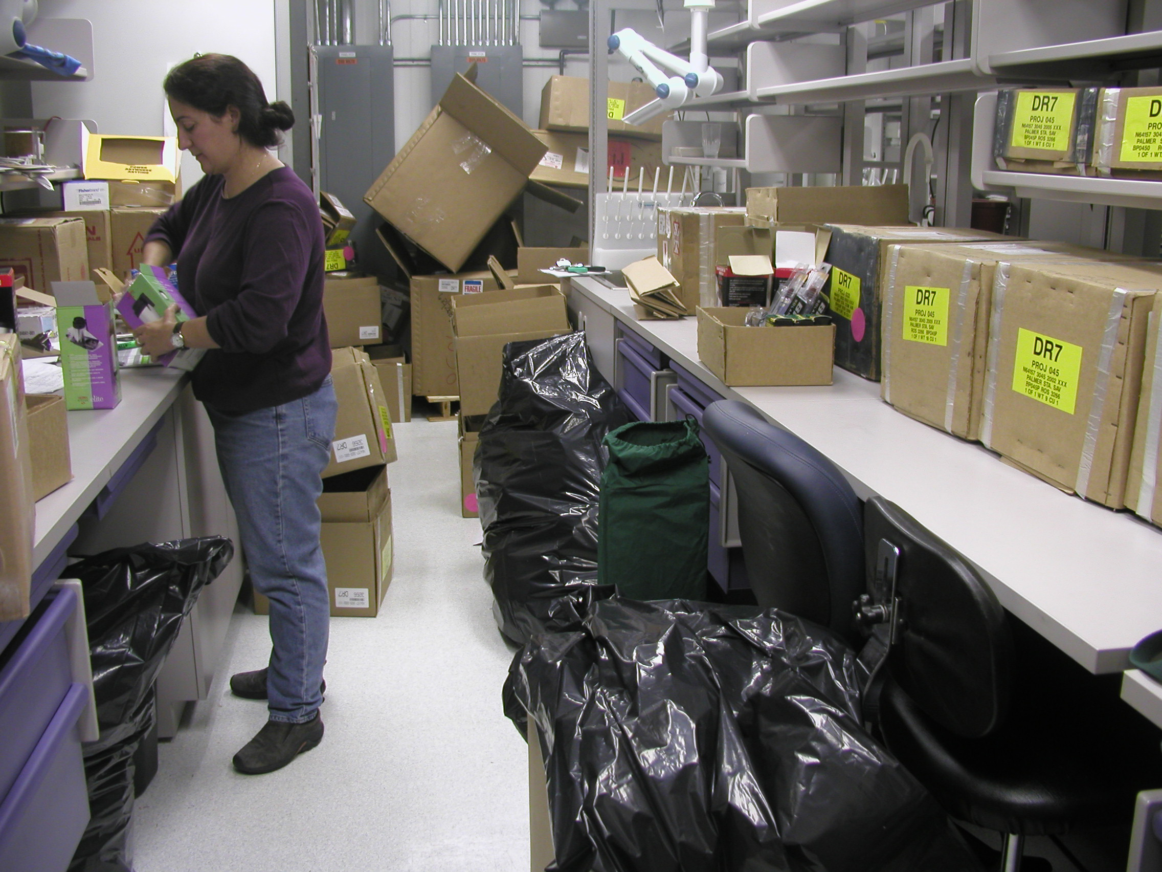 Woman unpacks cardboard boxes on long counter.