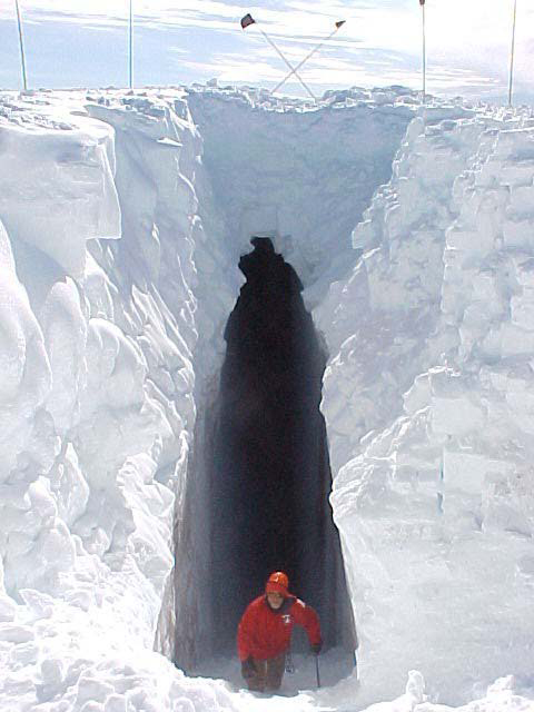 A man walks out from an enormous hole in the snow.