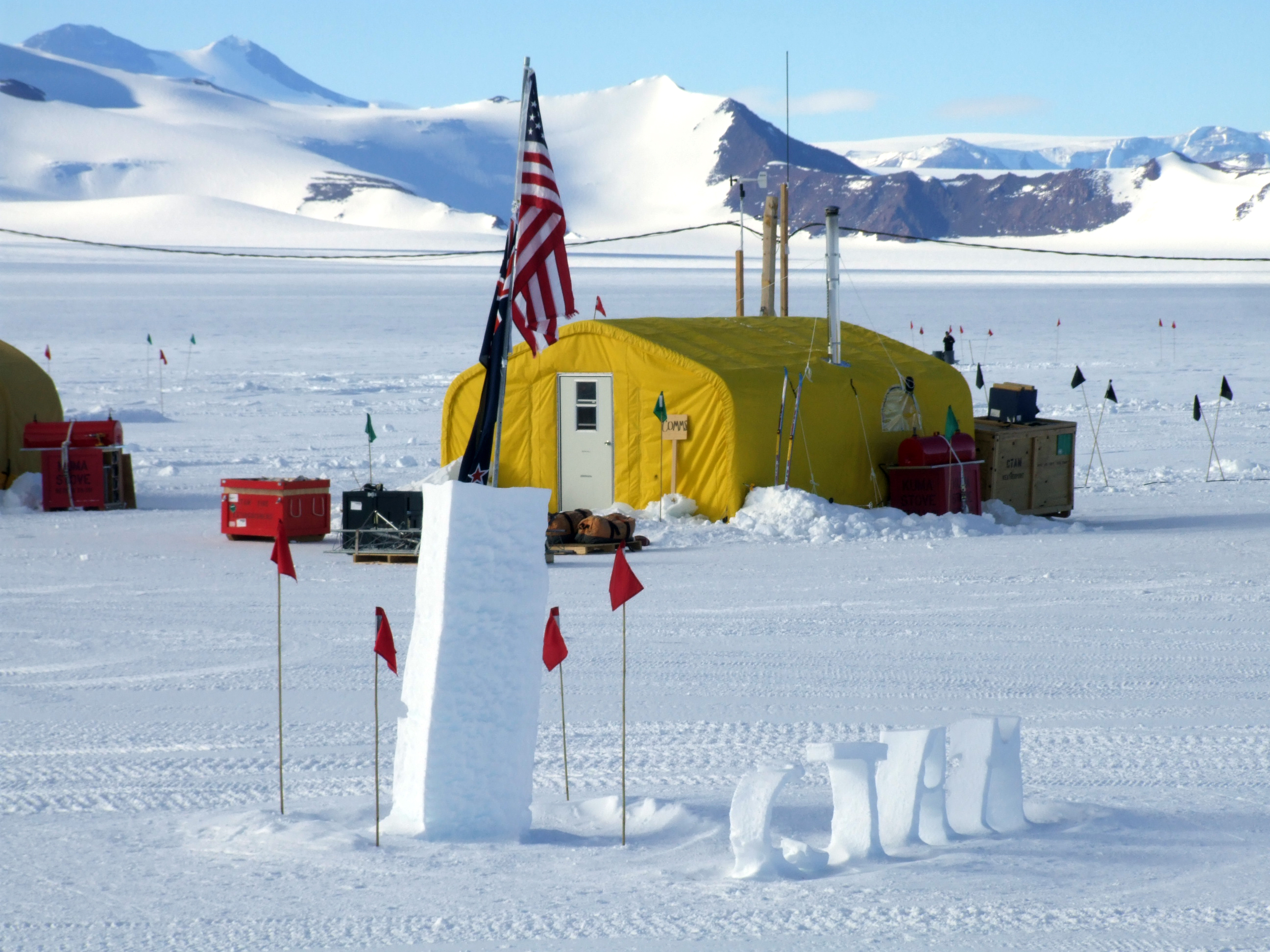 A yellow tent stands behind flags and snow sculpture.