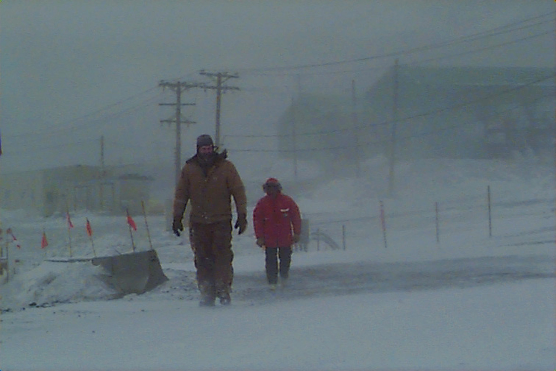 Two people walk in a blizzard.