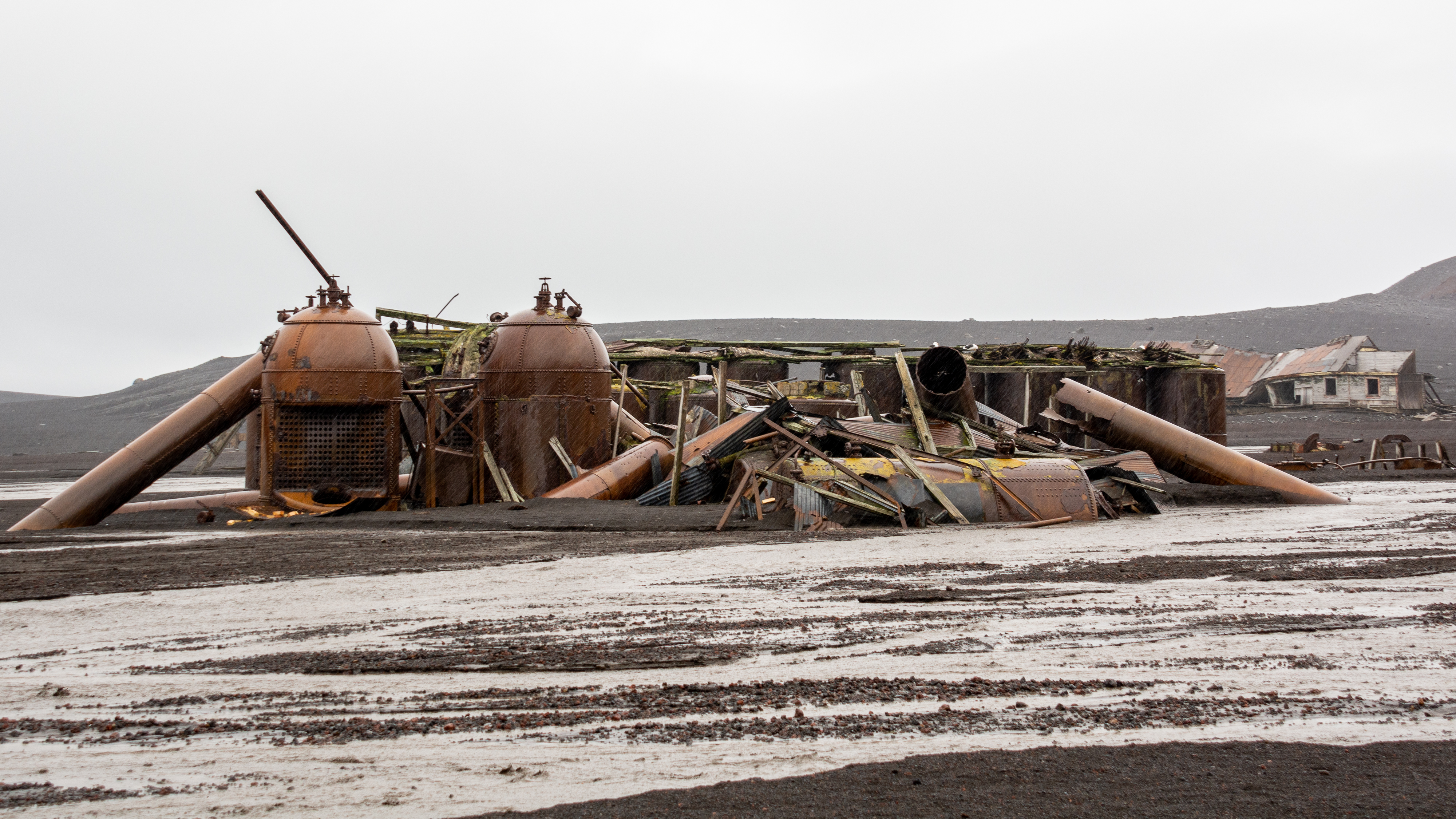 Rusting structures with a collapsed building in the background.