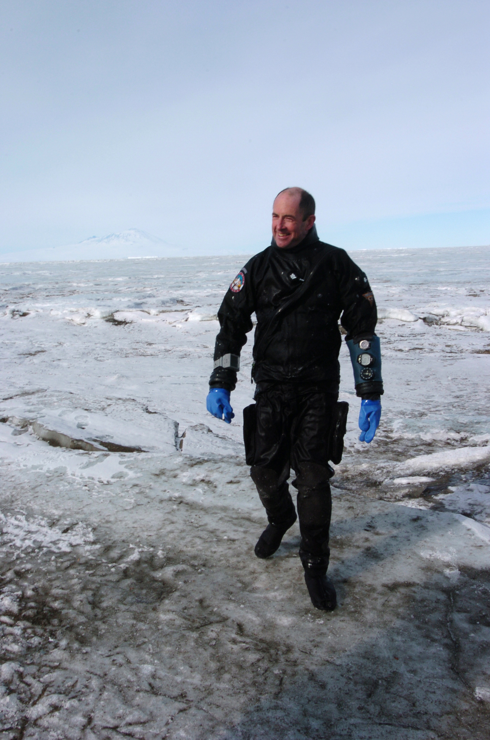 A man in a diving dry suit walks on ice.