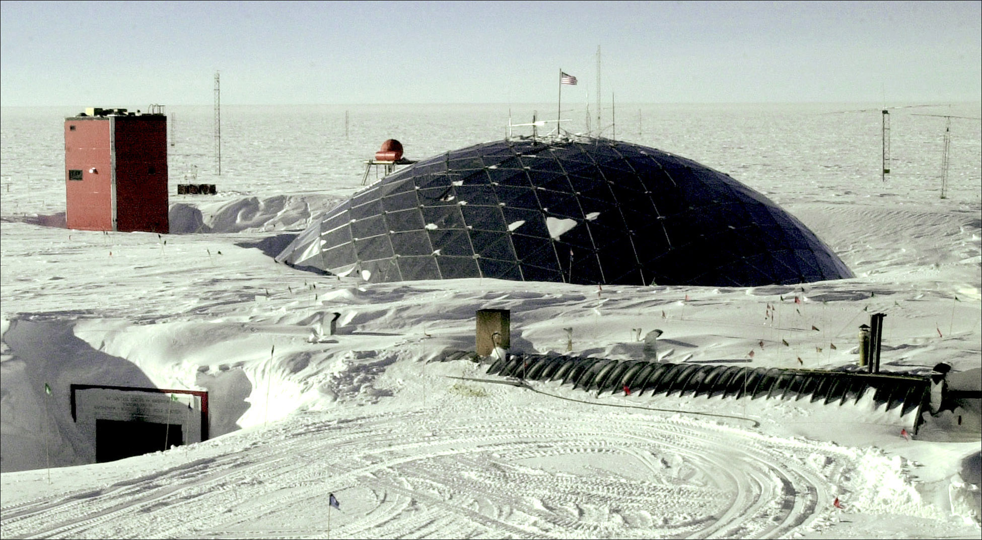 A large geodesic dome, mostly buried in snow, with a U.S. flag flying at the top.