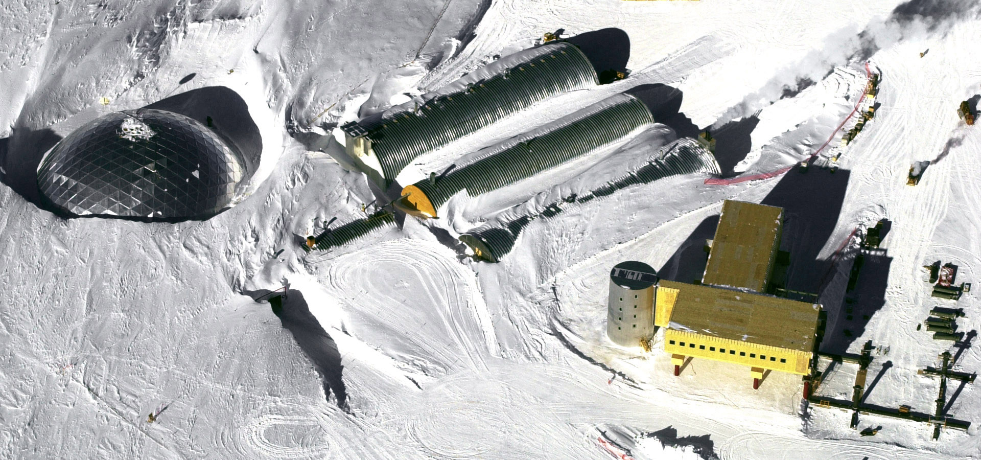 Aerial view of South Pole dome on left, three long corrugated steel buildings in the middle and a newly constructed building on the right.